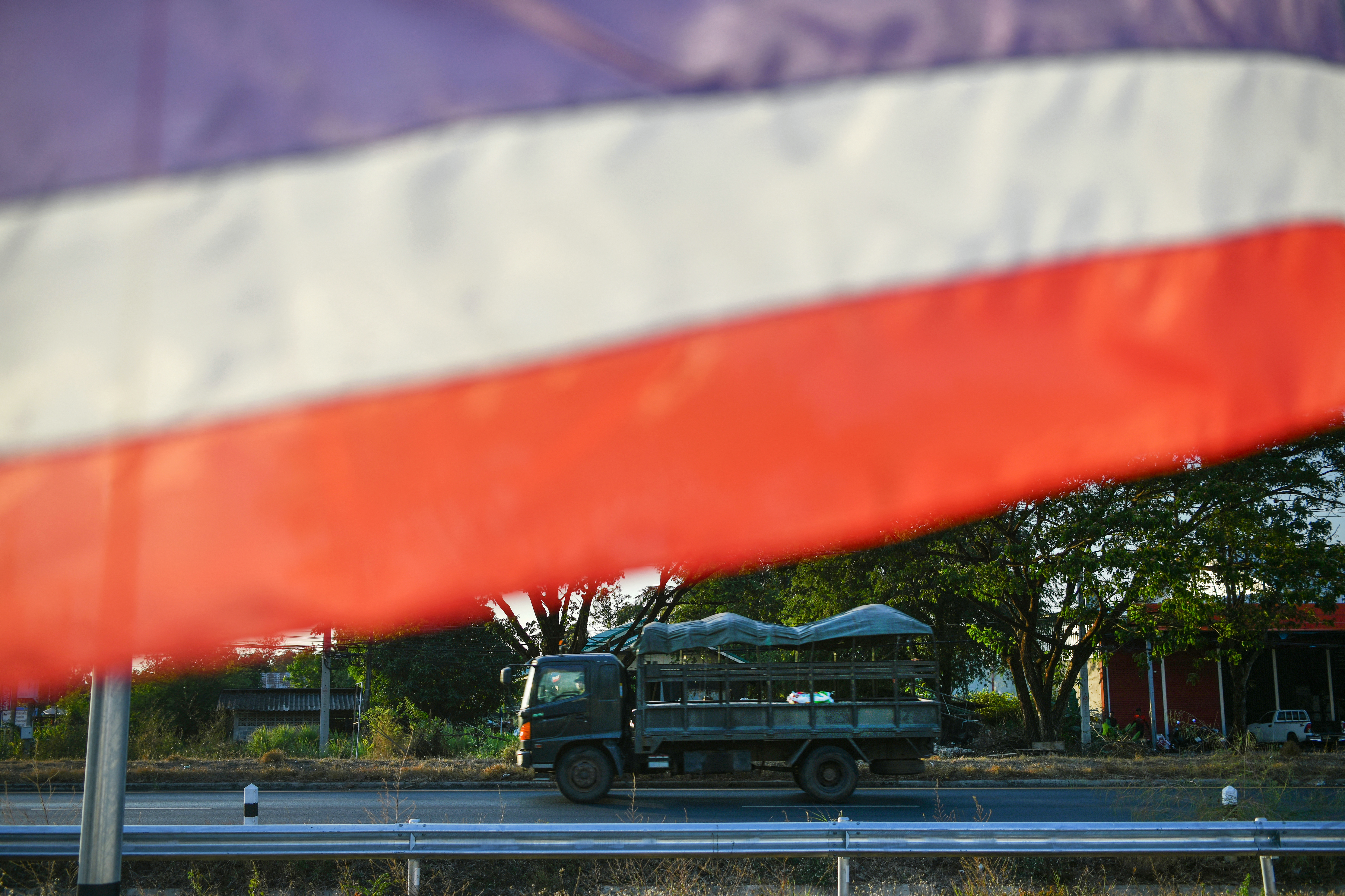 A Thai military vehicle passes by a Thai national flag.
