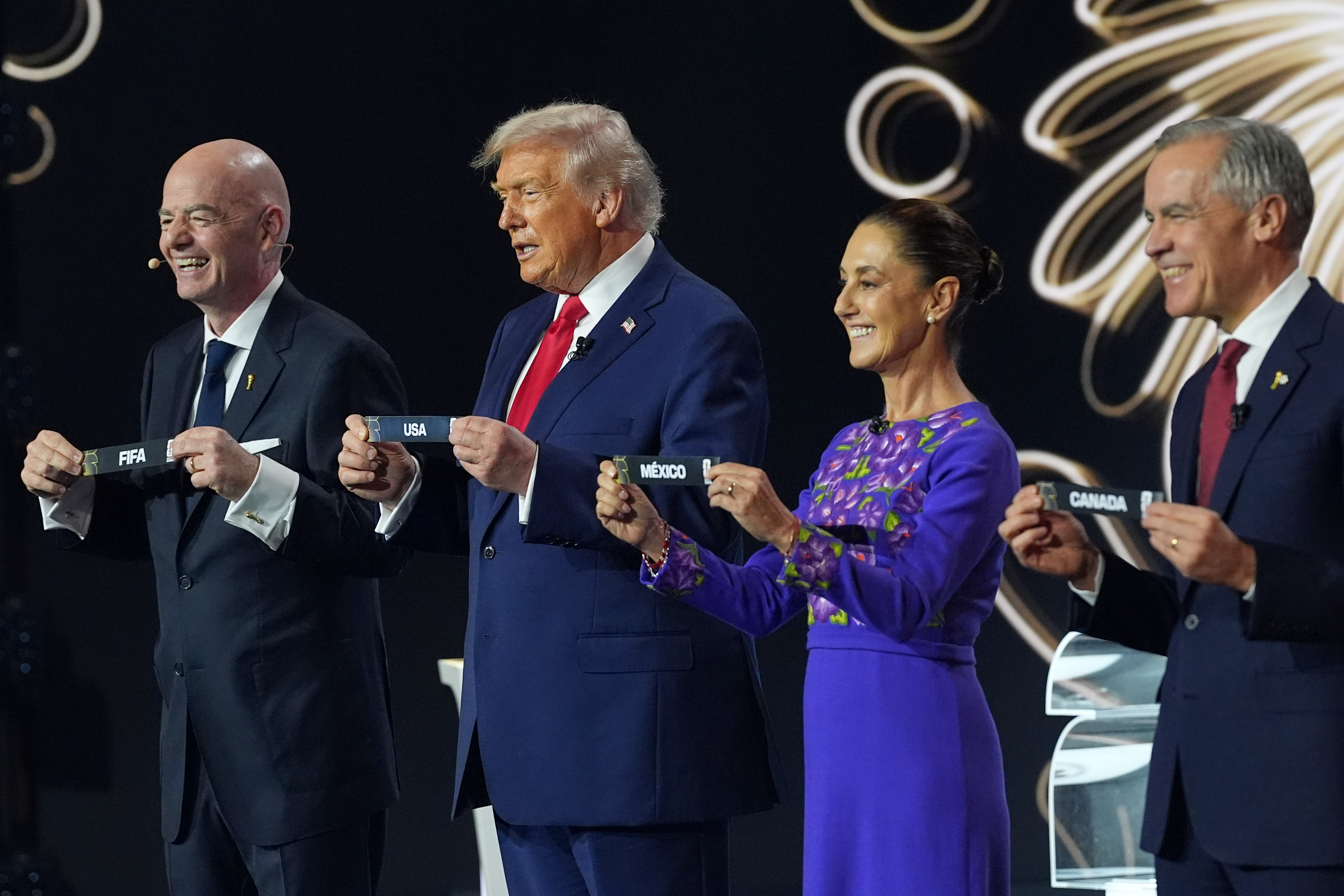 Canadian Prime Minister Mark Carney, Mexican President Claudia Sheinbaum, President Donald Trump and FIFA President Gianni Infantino hold up country names during the draw for the 2026 soccer World Cup at the Kennedy Center in Washington, Friday, Dec. 5, 2025. (AP Photo/Jacquelyn Martin)