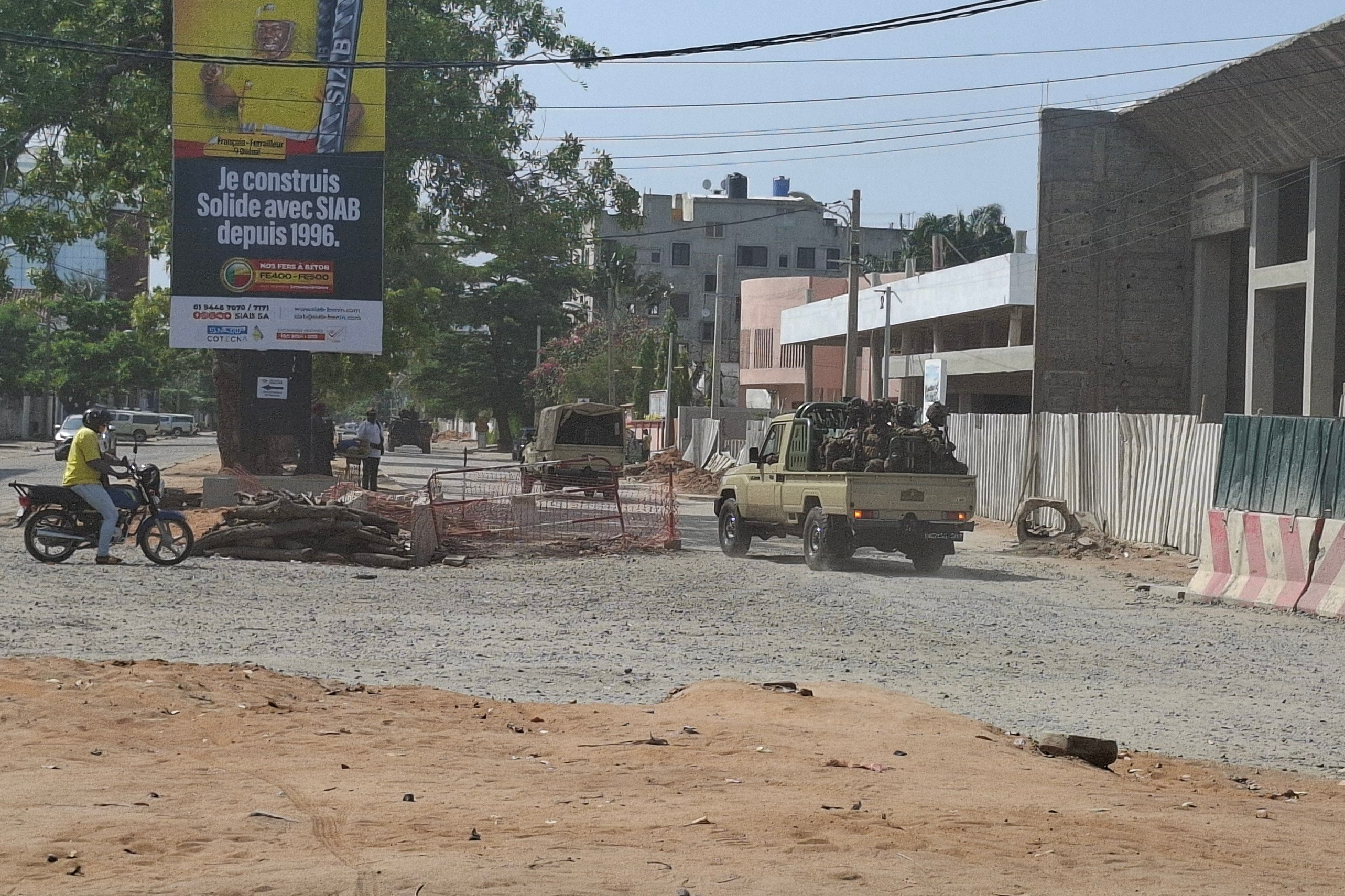 Soldiers ride in a military vehicle along a street.
