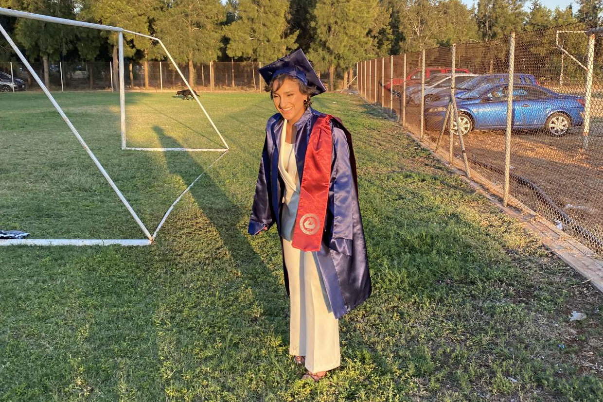 Young woman in cap and gown on a football pitch