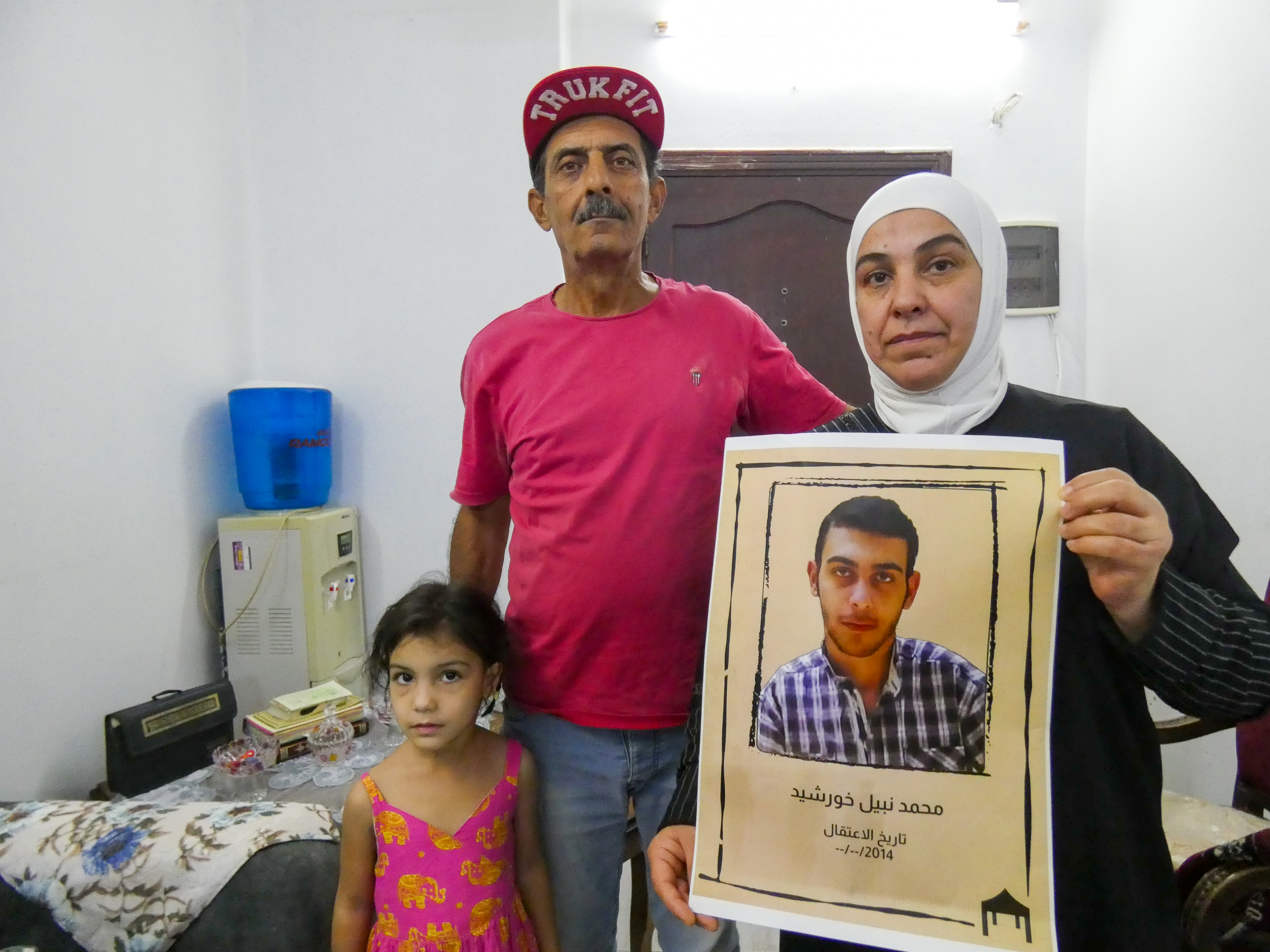 Safinaz Al Chaaibi with her husband Nabil, along with their granddaughter Sham in their live room holding a picture of Hamid.
