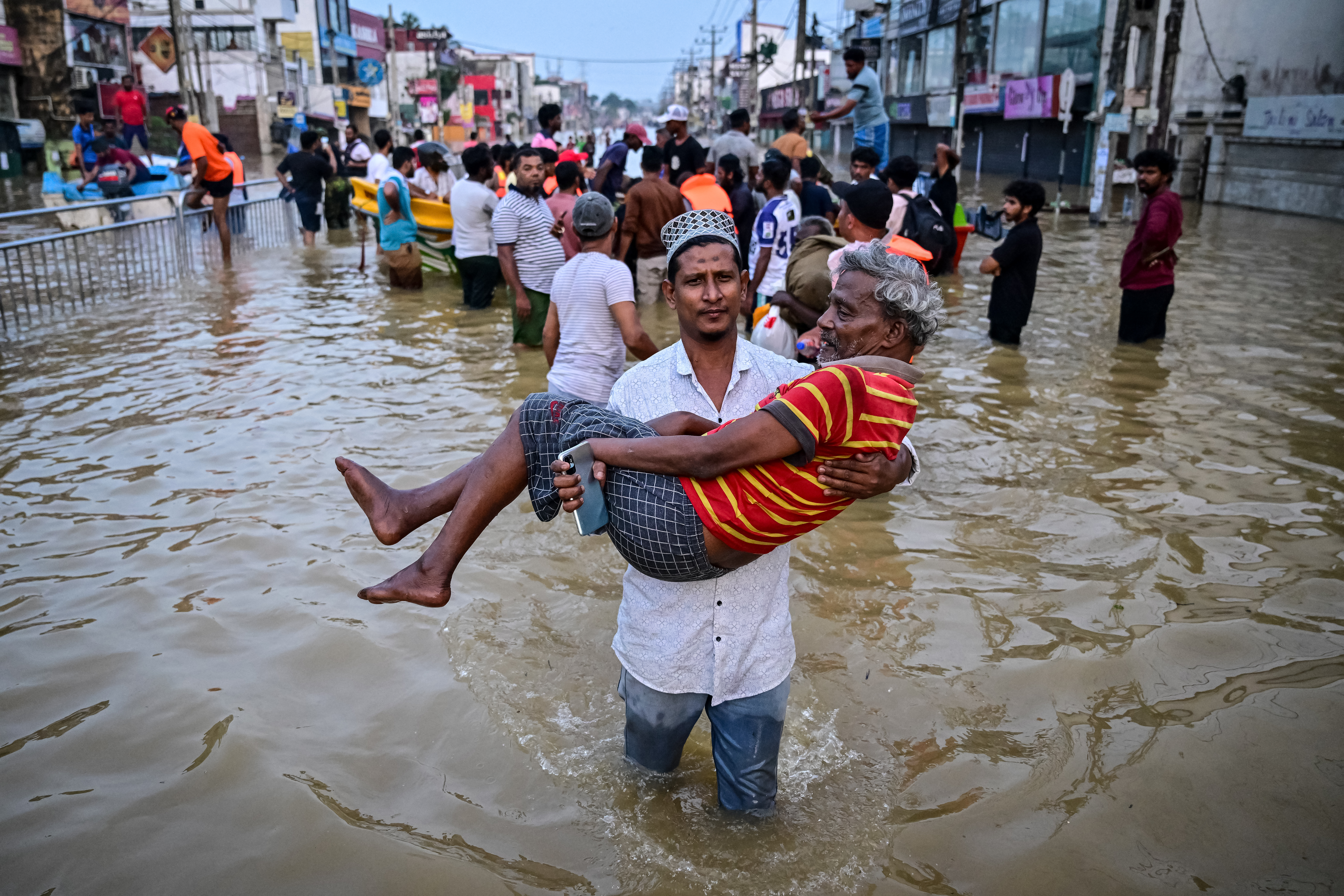 A youth carries an elderly man as they wade through a flooded street.