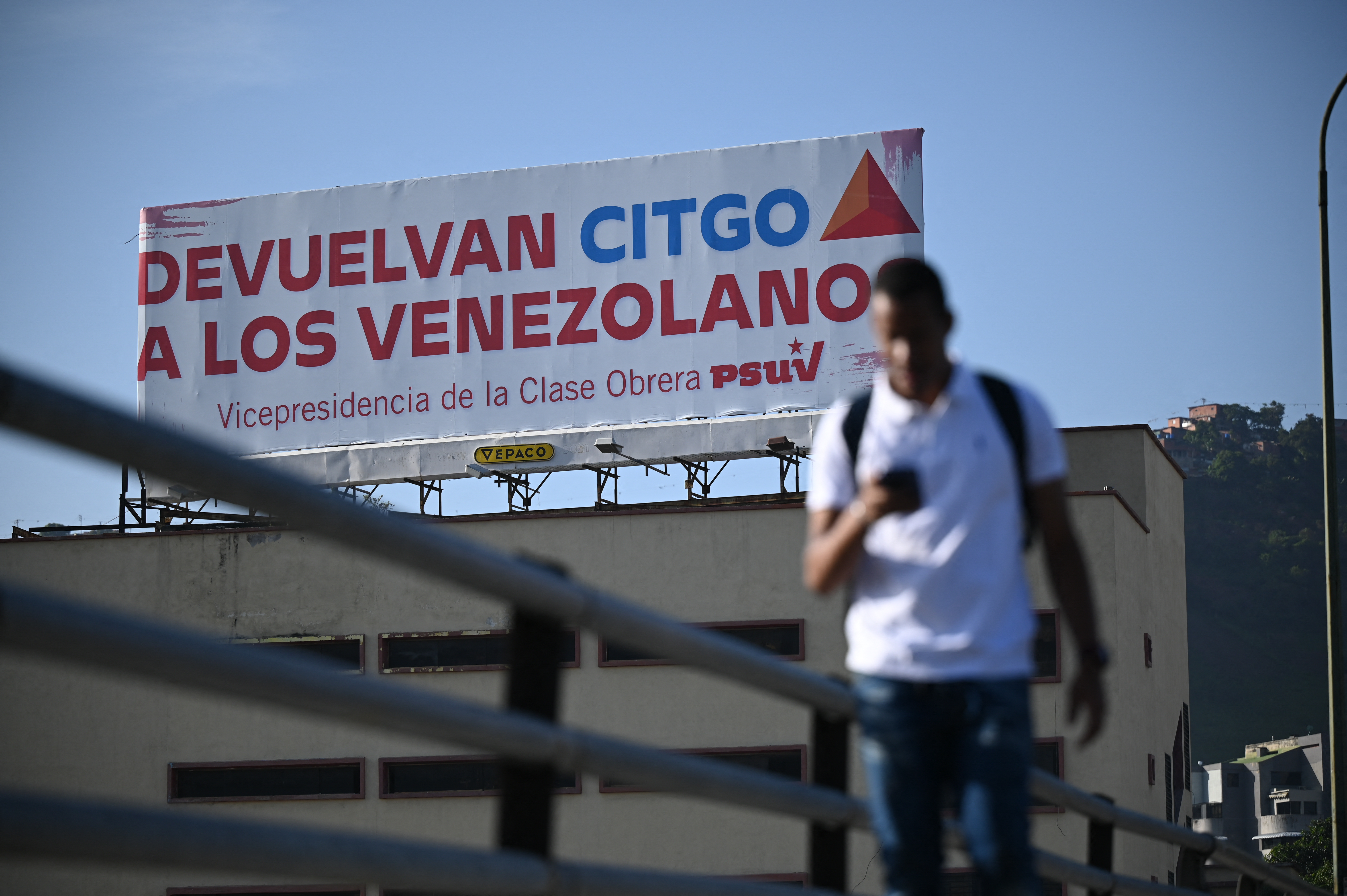 (FILES) A man walks past a billboard of the United Socialist Party of Venezuela (PSUV), reading "Return CITGO to the Venezuelans," in Caracas on June 27, 2023.