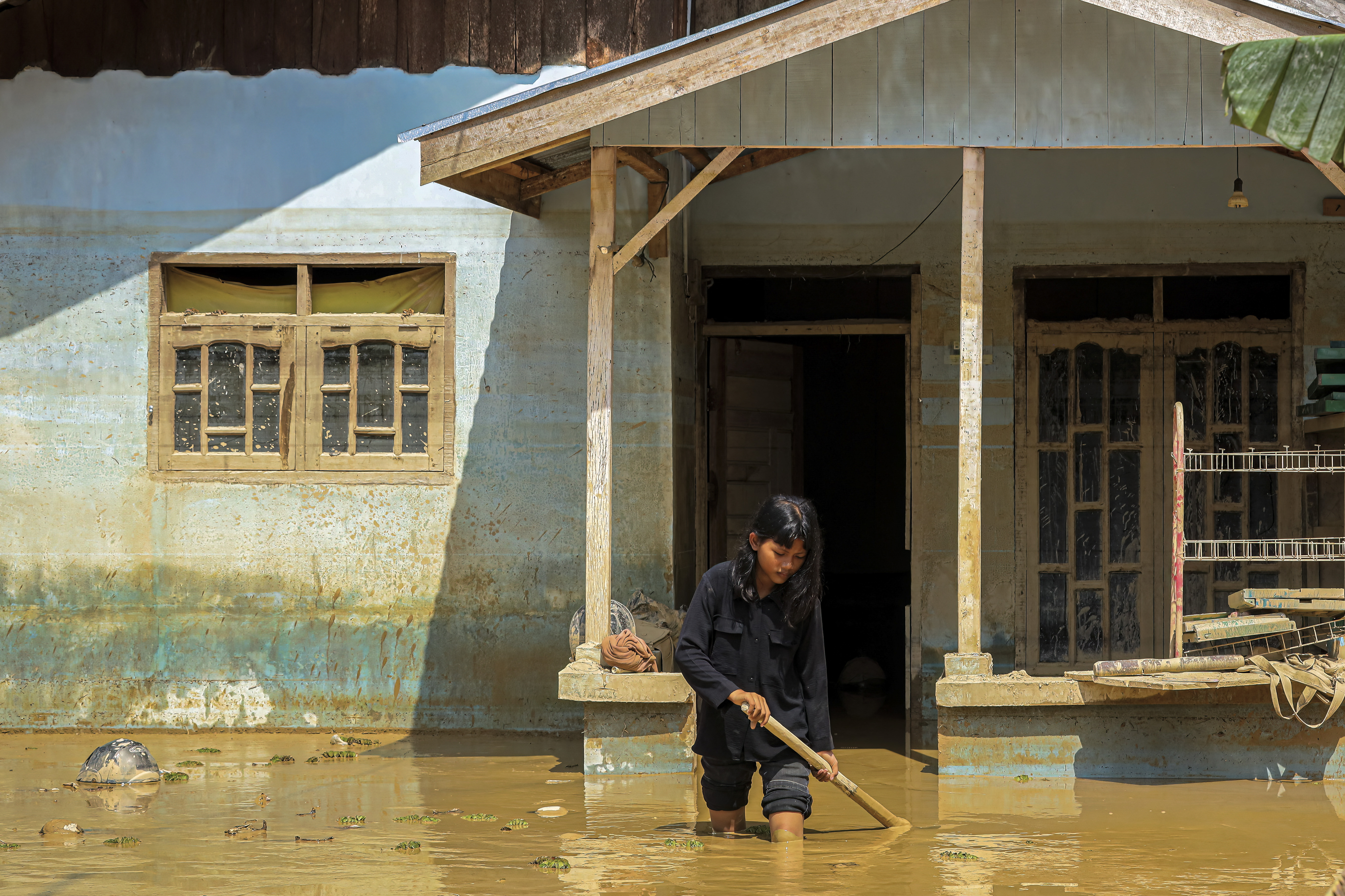 This picture taken on December 5, 2025 shows a young girl walking through mud in front of her house in a flood affected area in Aceh Tamiang, Aceh province.