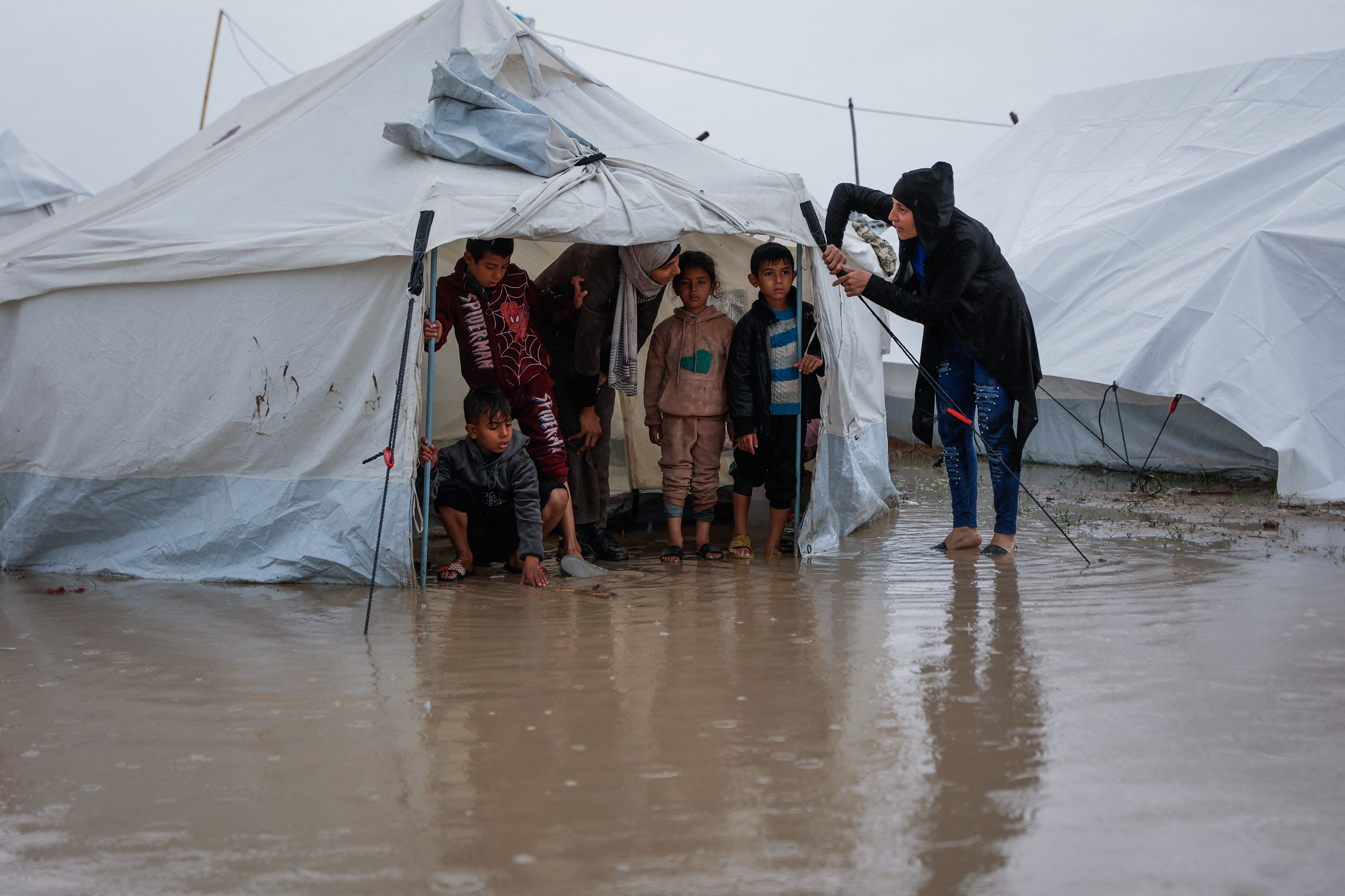 A woman fixes her tent as children stand inside at a makeshift camp sheltering displaced Palestinians after heavy rains in the Zeitoun neighbourhood of Gaza City on December 11, 2025.