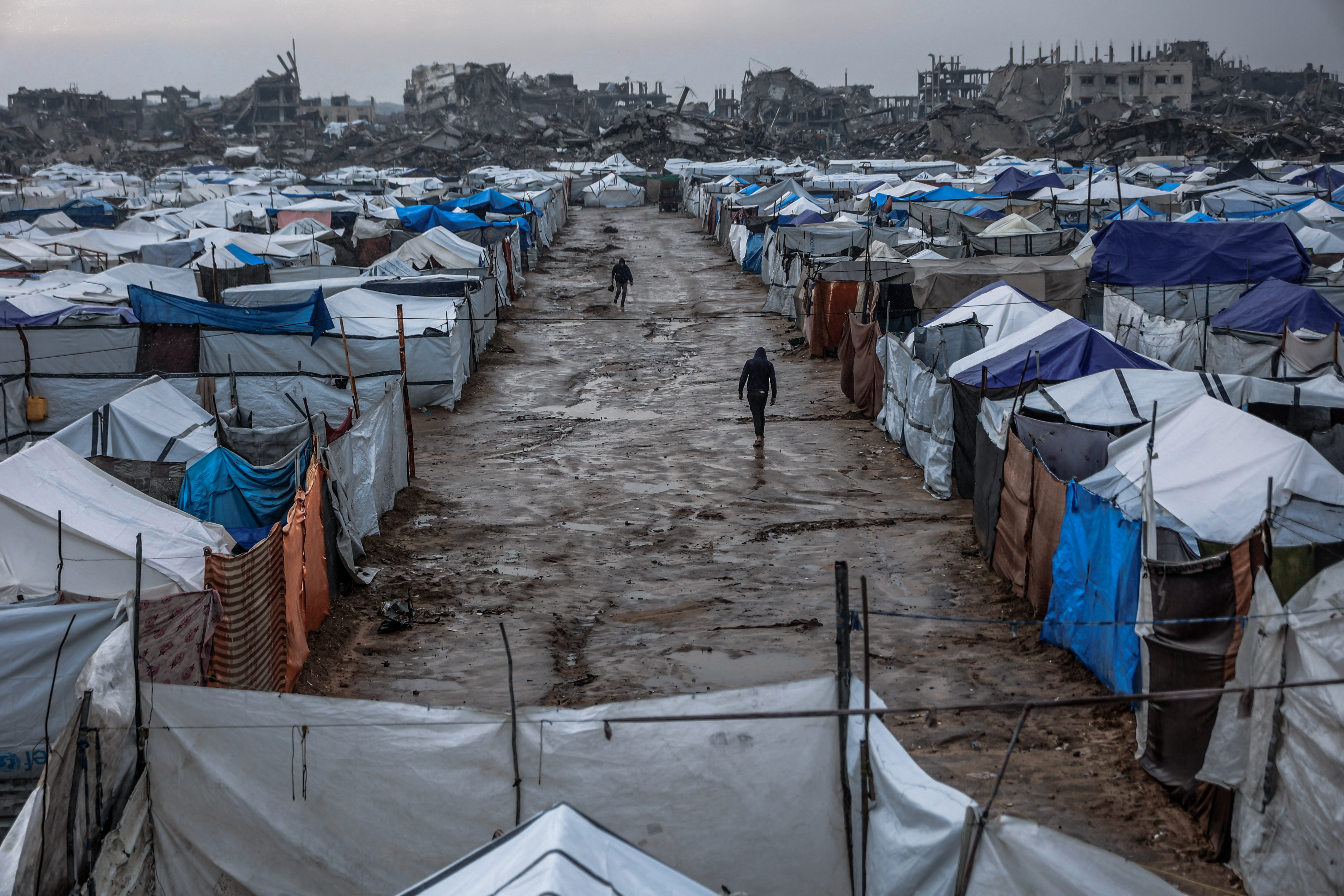 TOPSHOT - Men walk along a muddy alley at a makeshift camp sheltering displaced Palestinians after heavy rains in the Zeitoun neighbourhood of Gaza City on December 11, 2025.
