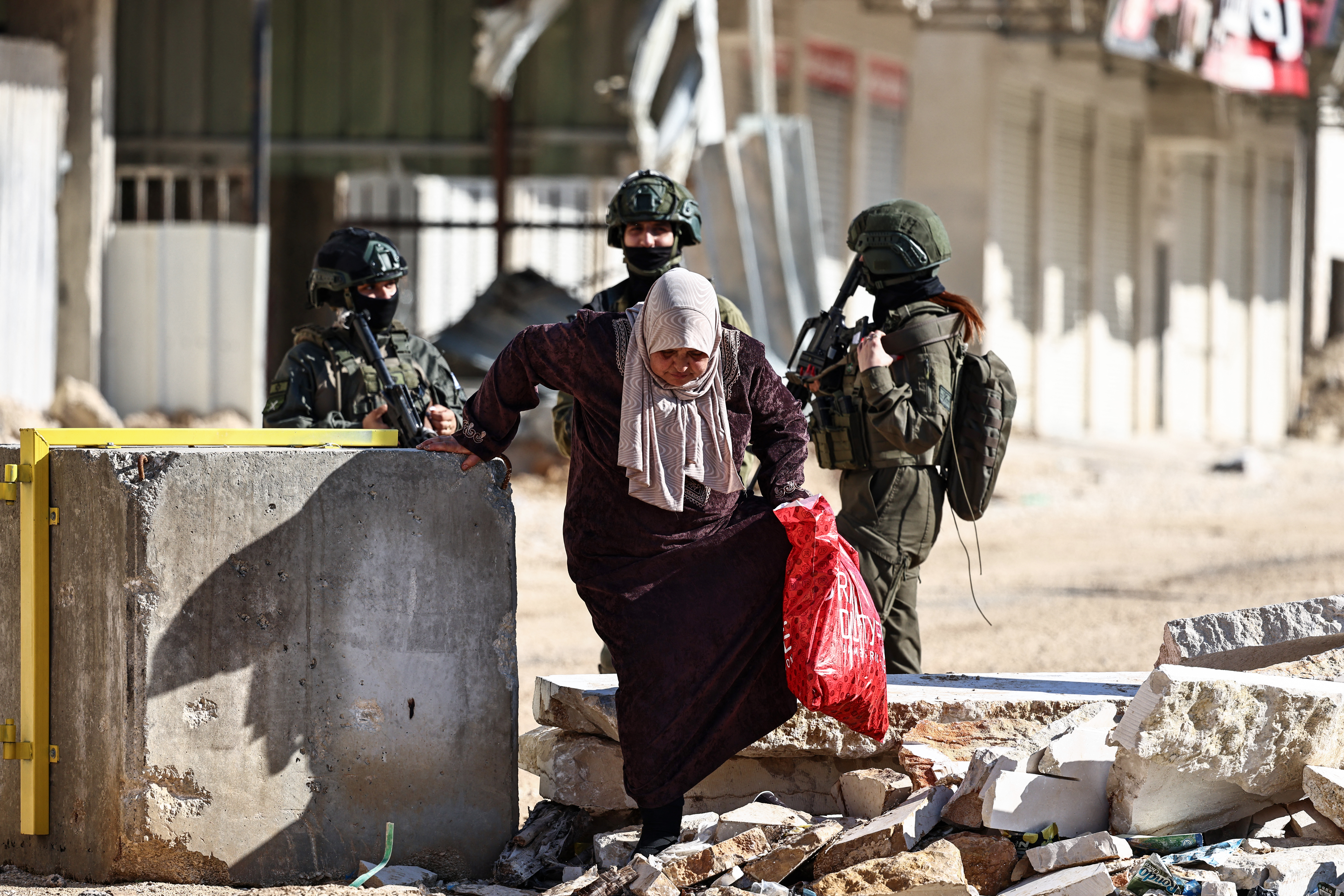 A resident of the Nur Shams refugee camp walks through concrete blocks while carrying belongings retrieved from her home ahead of the Israeli military’s demolition of residential buildings in the camp near Tulkarem in the Israeli-occupied West Bank on December 17, 2025.