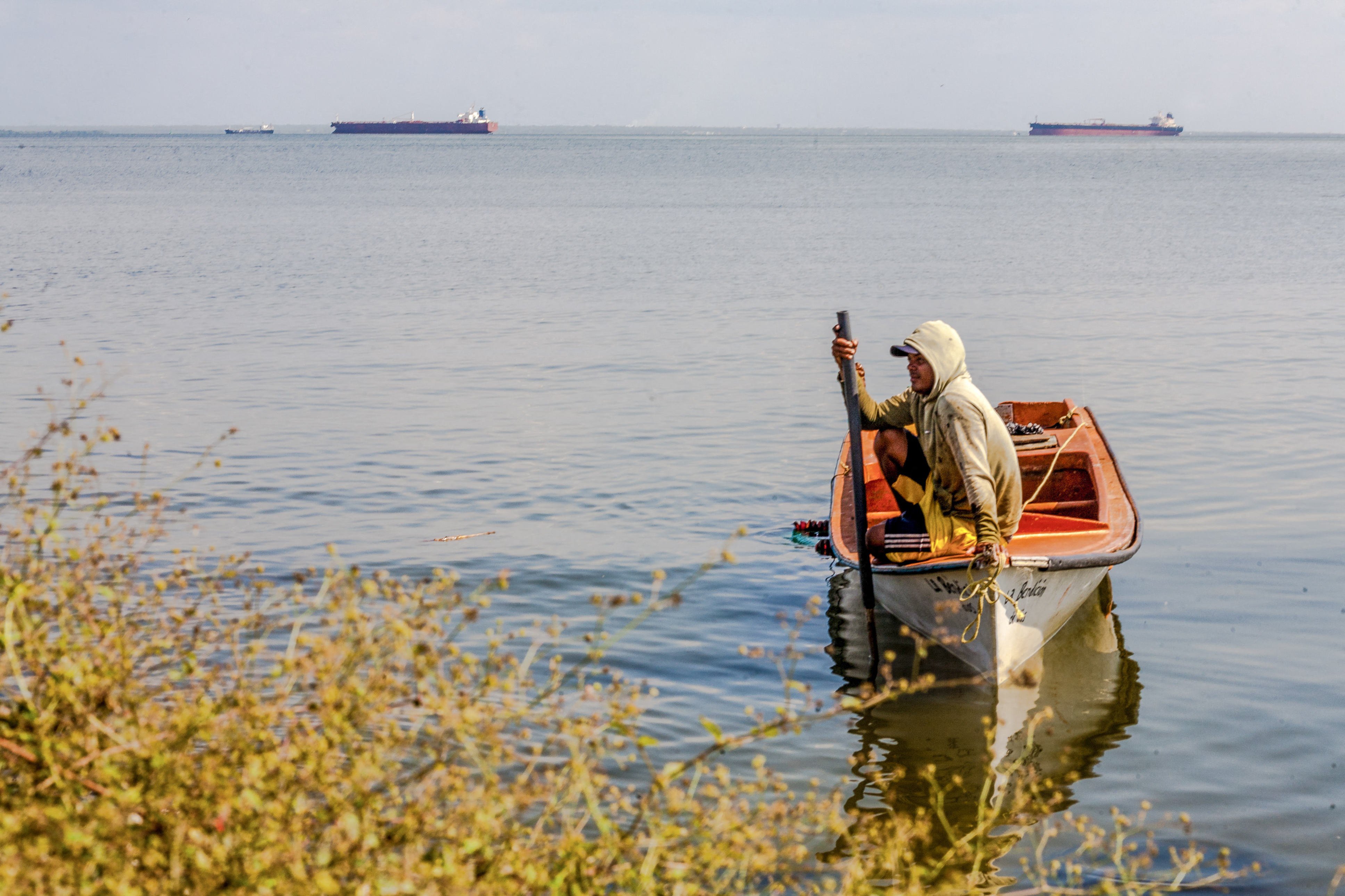 A man looks on at a boat with two crude oil tankers in the background on Lake Maracaibo, near Maracaibo, Zulia state, Venezuela on December 17, 2025.