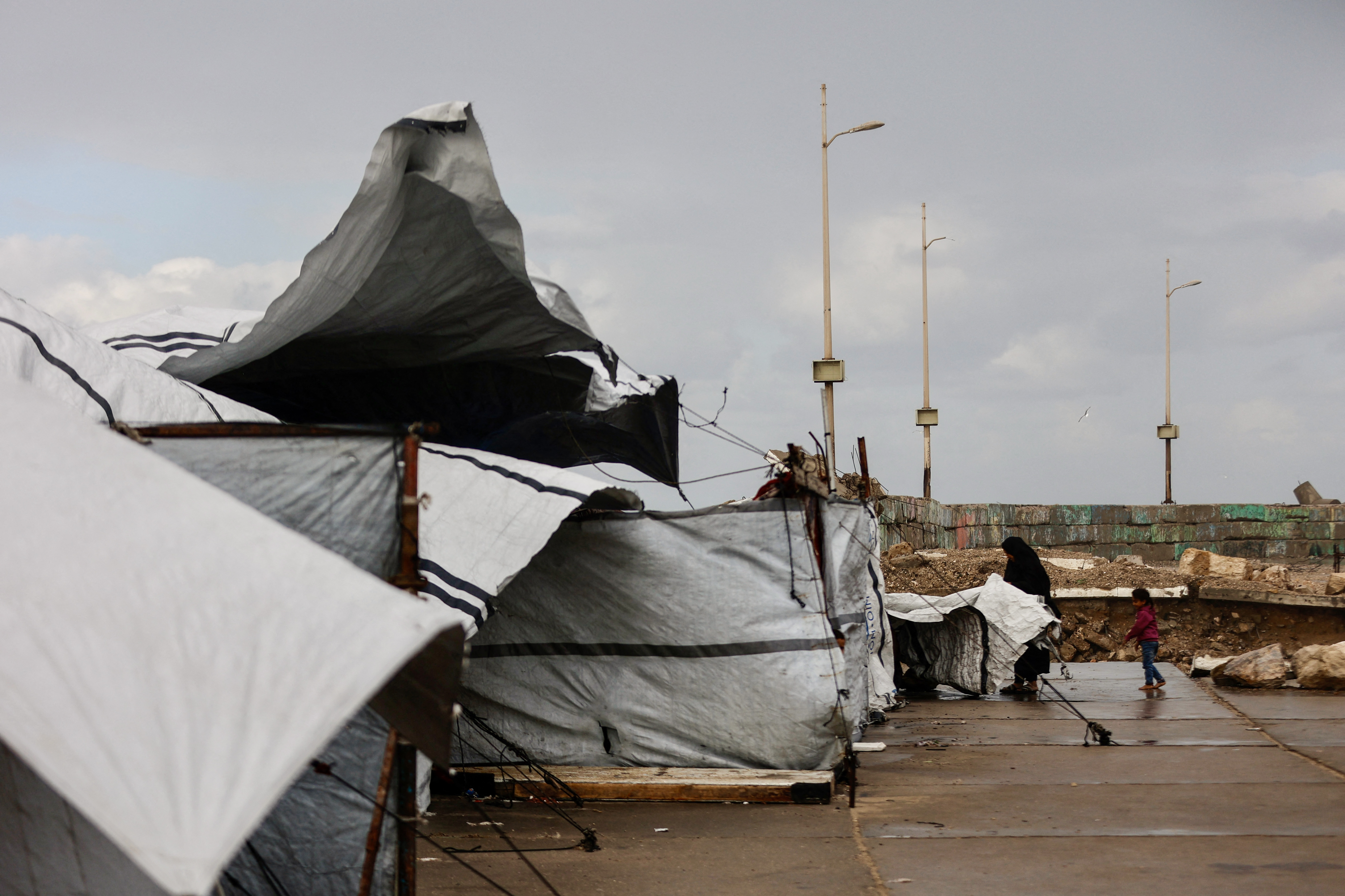 A displaced Palestinian woman adjusts the canvas of the family tent shelter as the region experiences rain and cold winter conditions, in Gaza City on December 28, 2025.