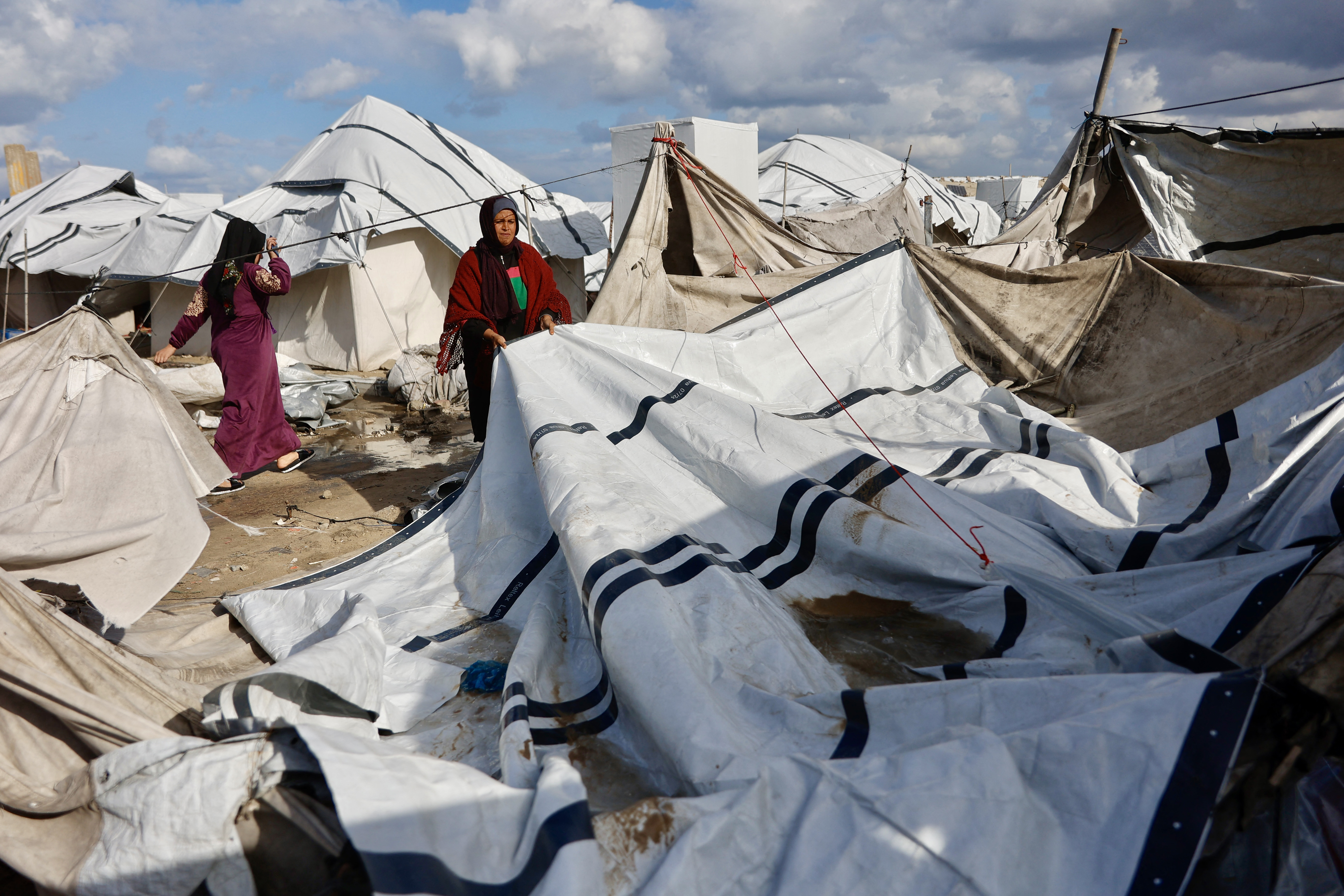A displaced Palestinian woman adjusts the canvas of the family tent shelter