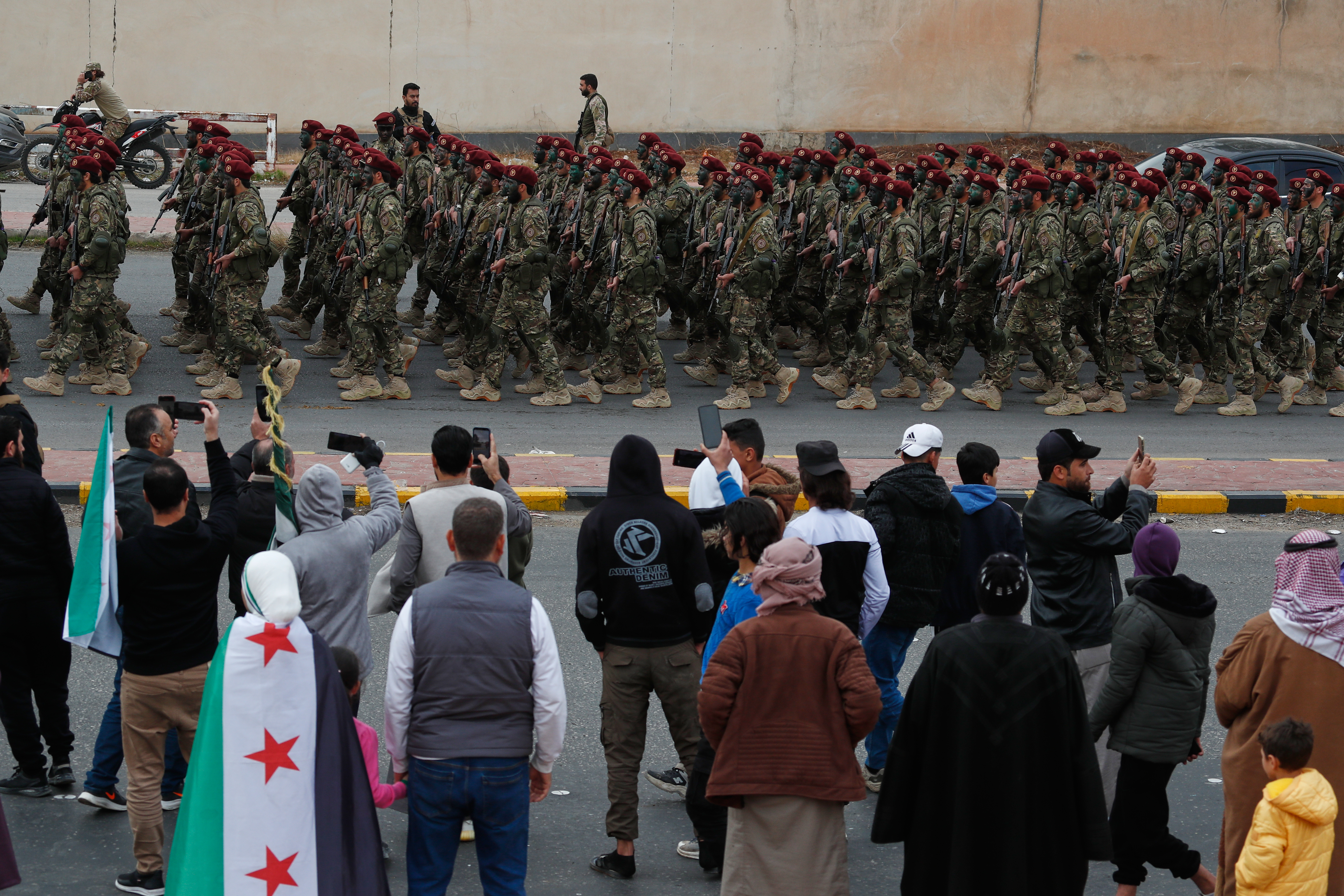 People watch and film as fighters from the new Syrian army march during celebrations marking the first anniversary of the ousting of former President Bashar Assad in Damascus, Syria, Monday, Dec. 8, 2025. (AP Photo/Omar Sanadiki)