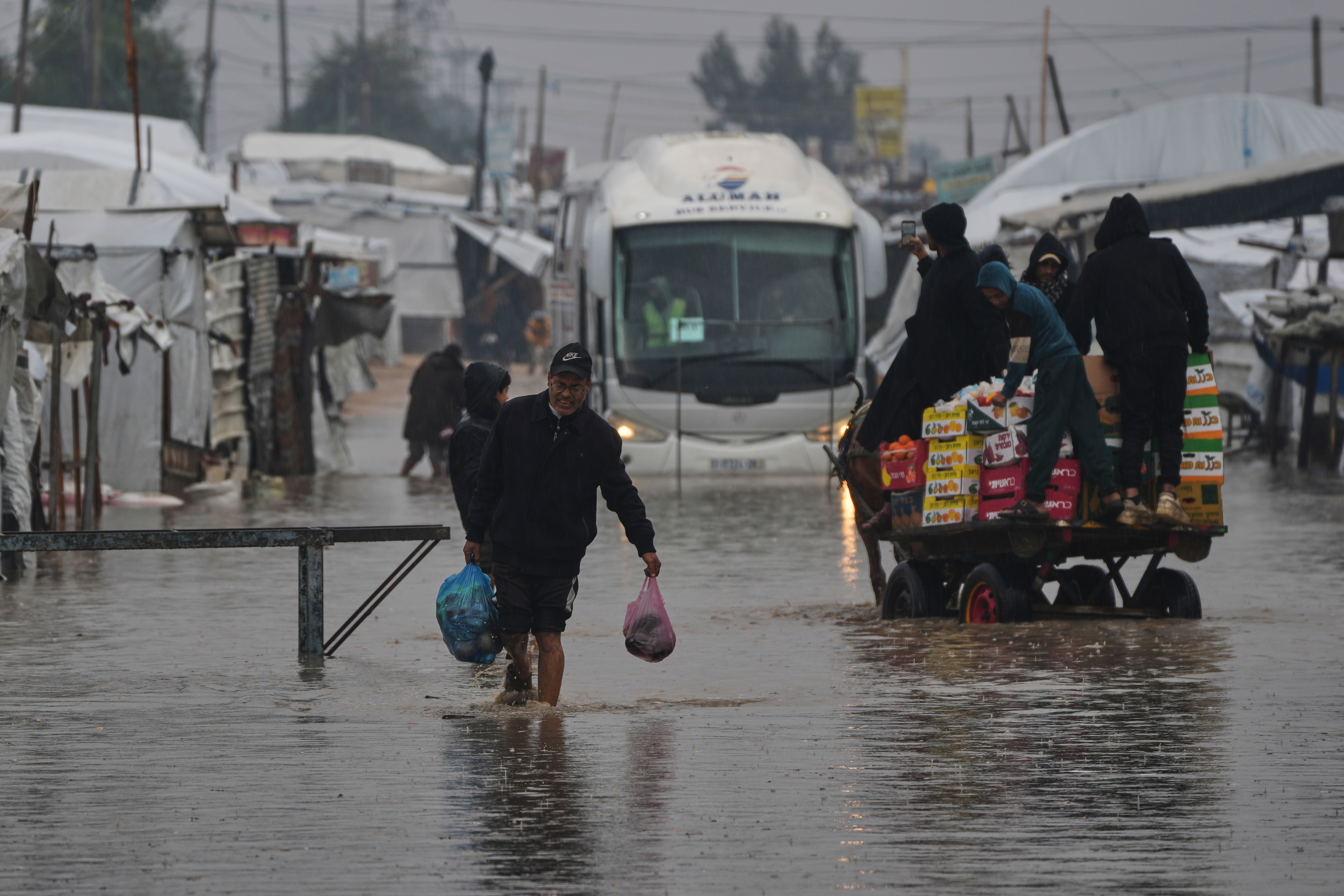 Palestinians walk through a flooded street following heavy rain in Khan Younis, southern Gaza Strip, Thursday, Dec. 11, 2025. (AP Photo/Abdel Kareem Hana)