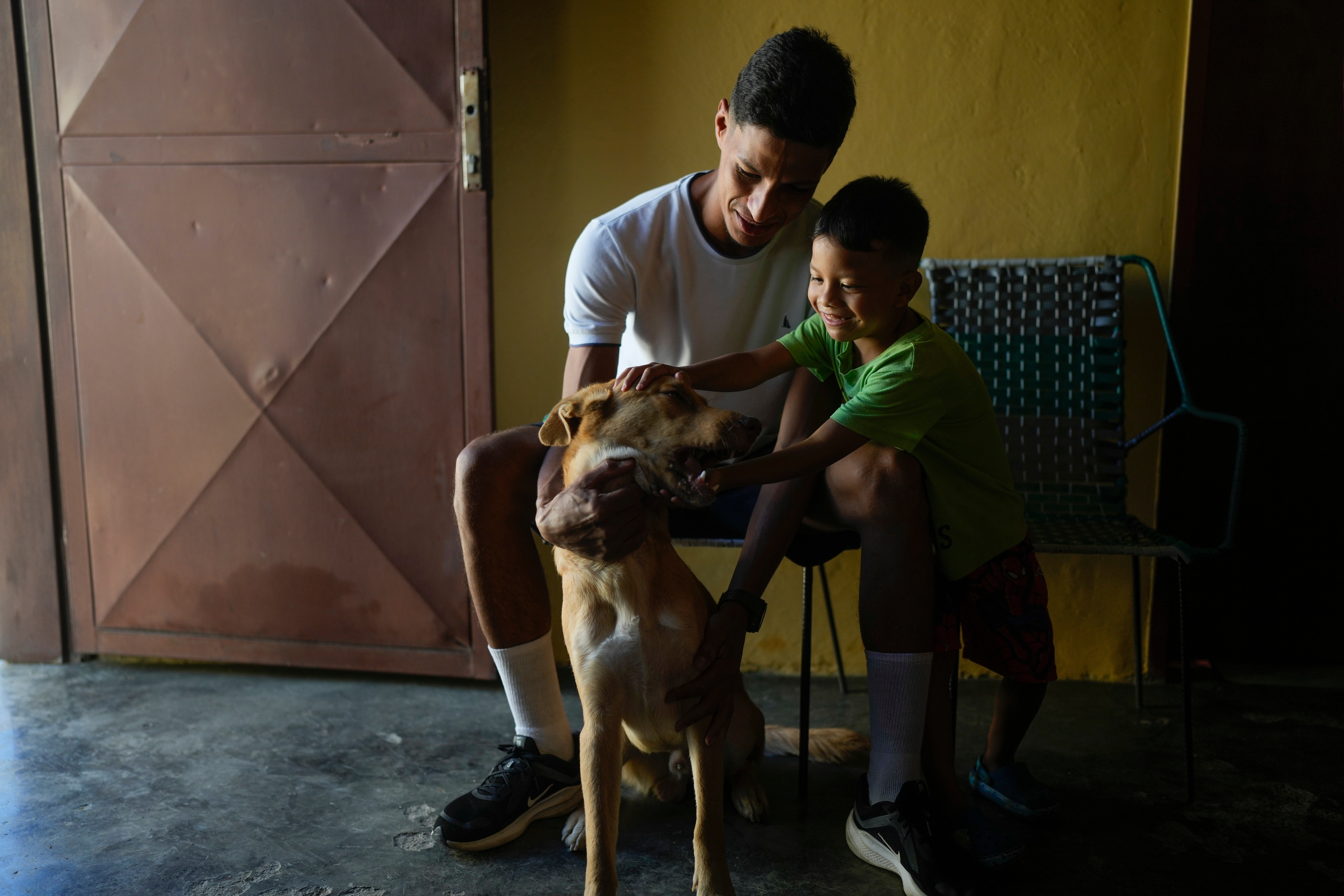 Abraham Castro and his partner's son Mathias pet the family dog ahead of Christmas Eve celebrations in Maracay, Venezuela, Thursday, Dec. 24, 2025. The Venezuelan migrant family adopted the dog as a puppy in Mexico before abandoning their journey to the United States and returning home following President Donald Trump's immigration crackdown. (AP Photo/Matias Delacroix)