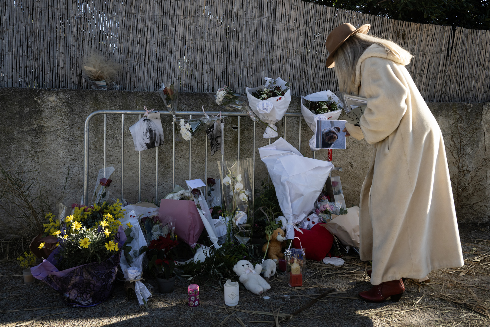 A woman stands next to flowers displayed on barriers at the entrance of "La Madrague" house, property of late Brigitte Bardot in Saint-Tropez, southeastern France on Dec. 29, 2025. [Miguel Medina/AFP]