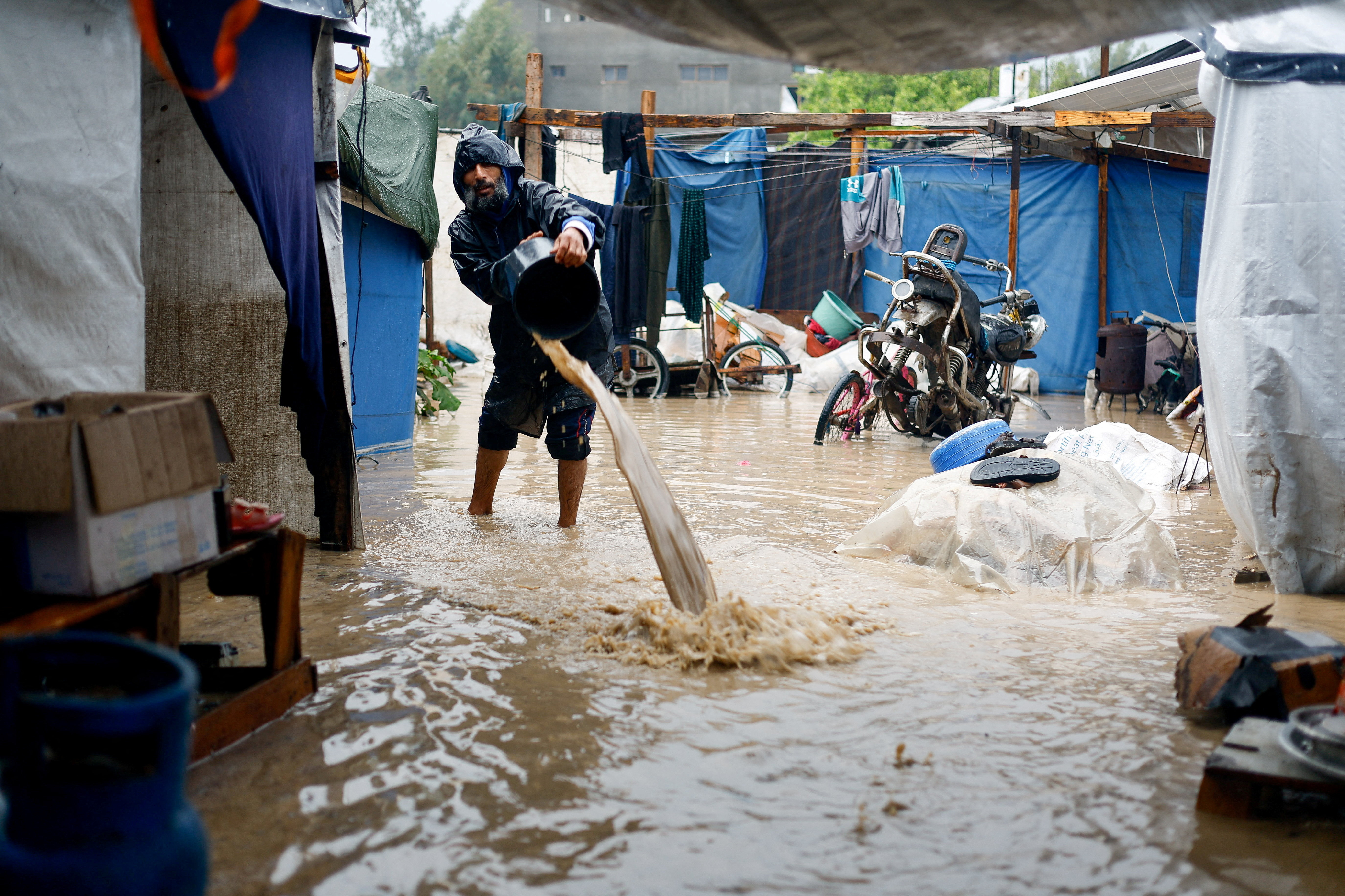 A displaced Palestinian man clears muddy water in a flooded tent camp on a rainy day in Nuseirat, central Gaza Strip, December 12, 2025. [Mahmoud Issa/Reuters]