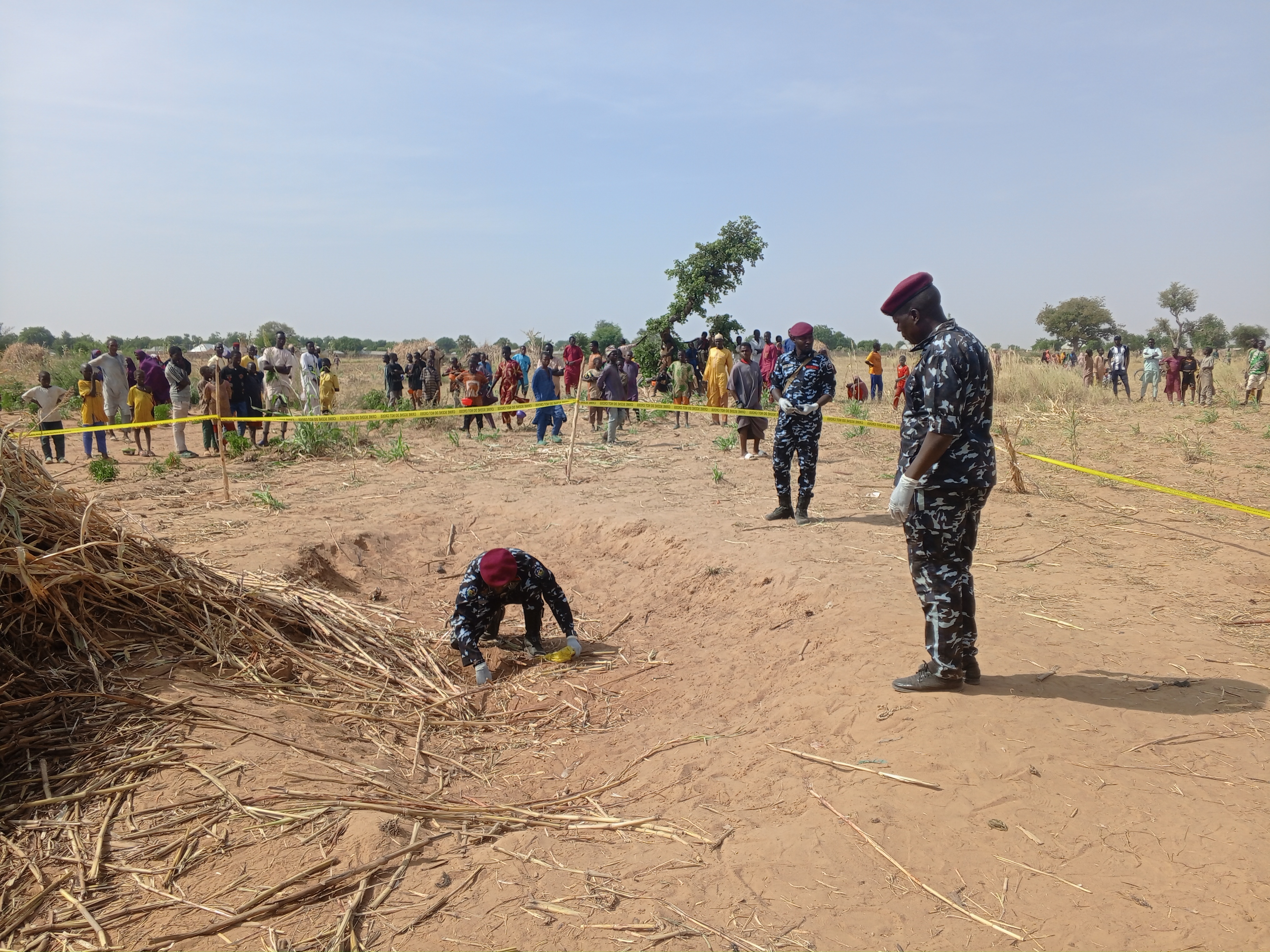 Police officer inspects a hole in the sandy ground inside area barricaded with yellow tape.