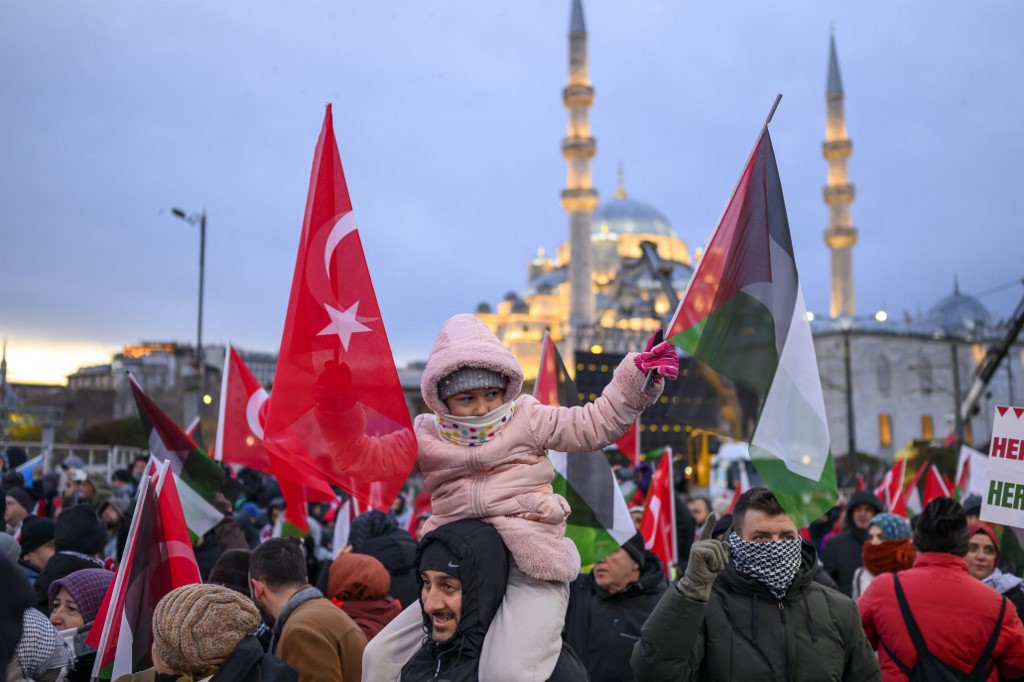 A young girl holds Turkish and Palestinian flags as people demonstrate.