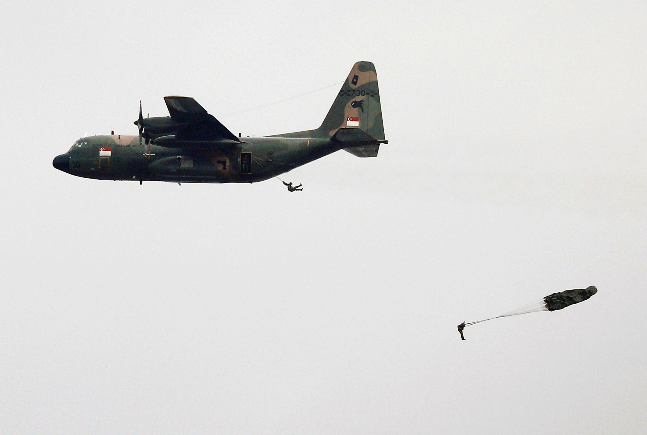 Paratroopers jump out of an aircraft in their parachutes.