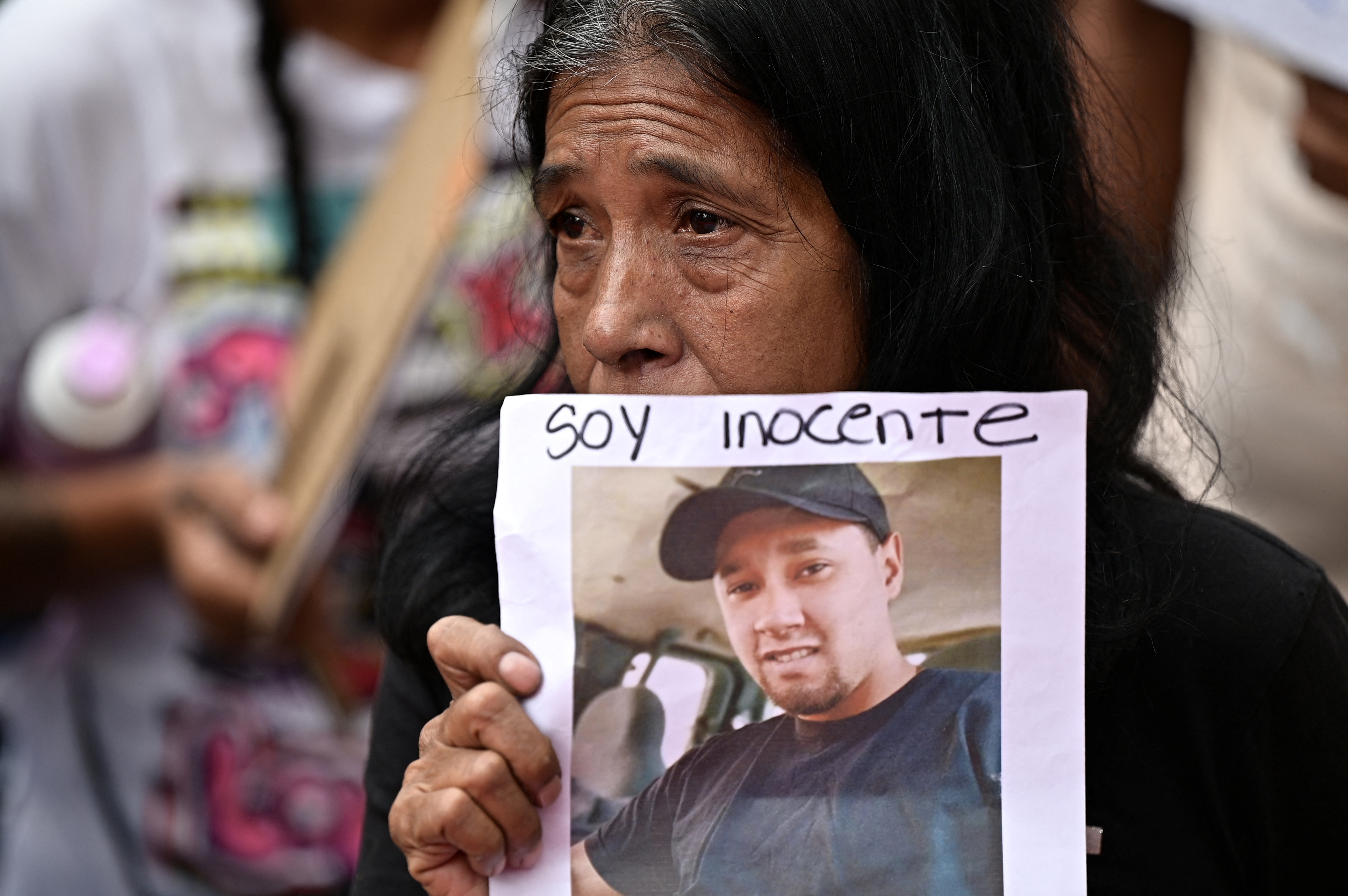 A crying woman holds up a photo of her son with the words, "Soy Inocente"