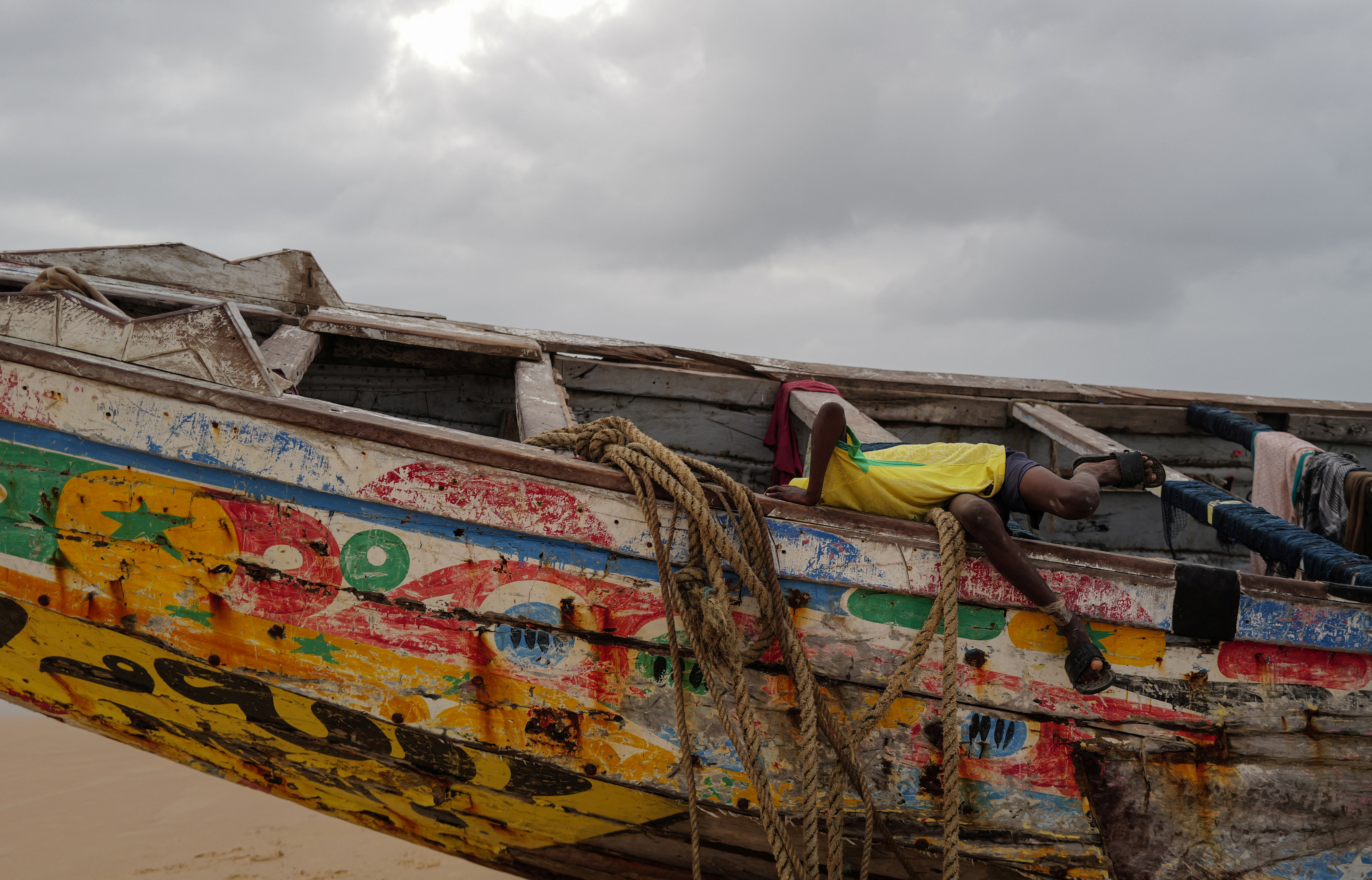 A boy plays in a pirogue used to transport migrants and asylum seekers from The Gambia, in Senegal