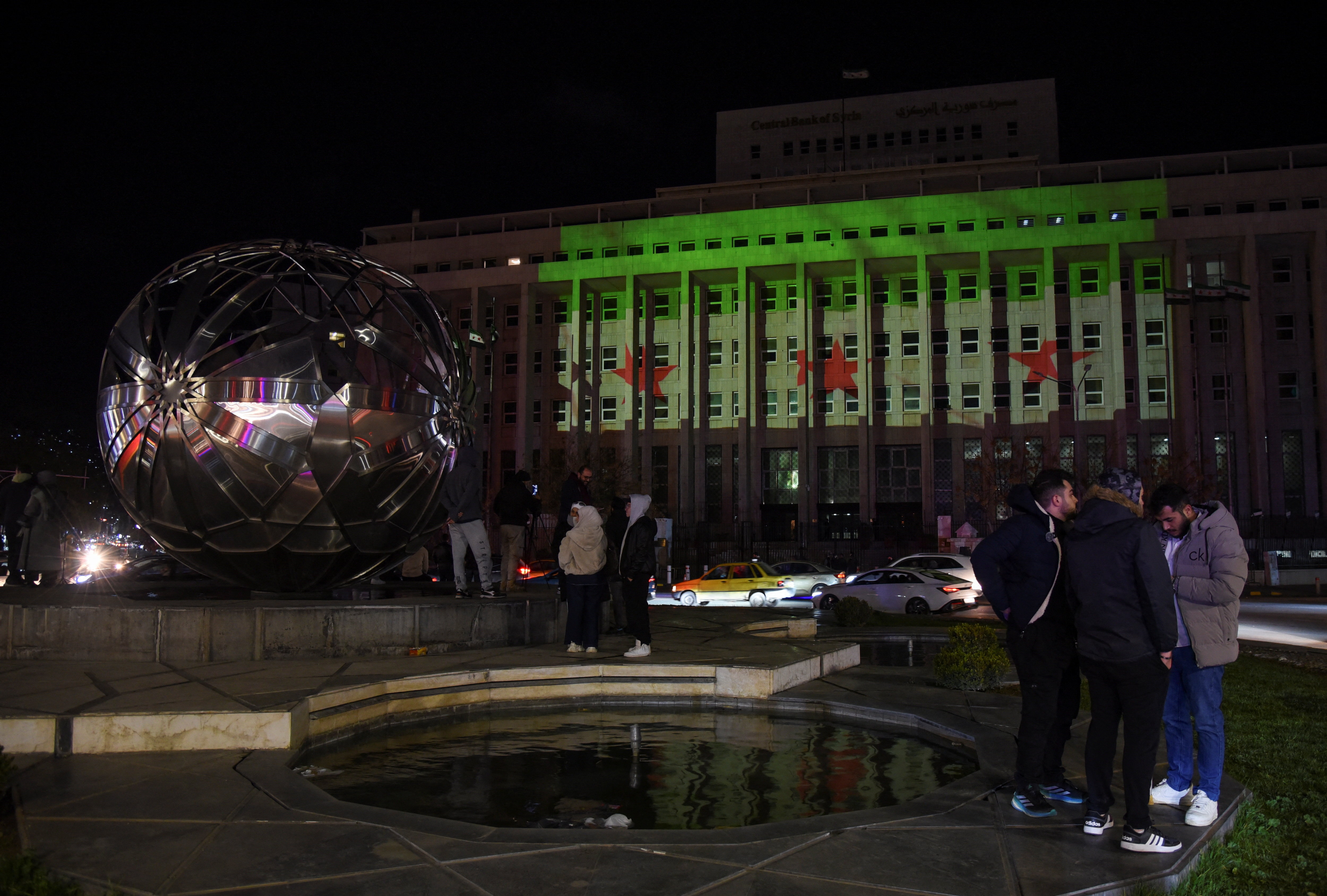 People stand near the building of the Central Bank of Syria as the national flag is projected on it