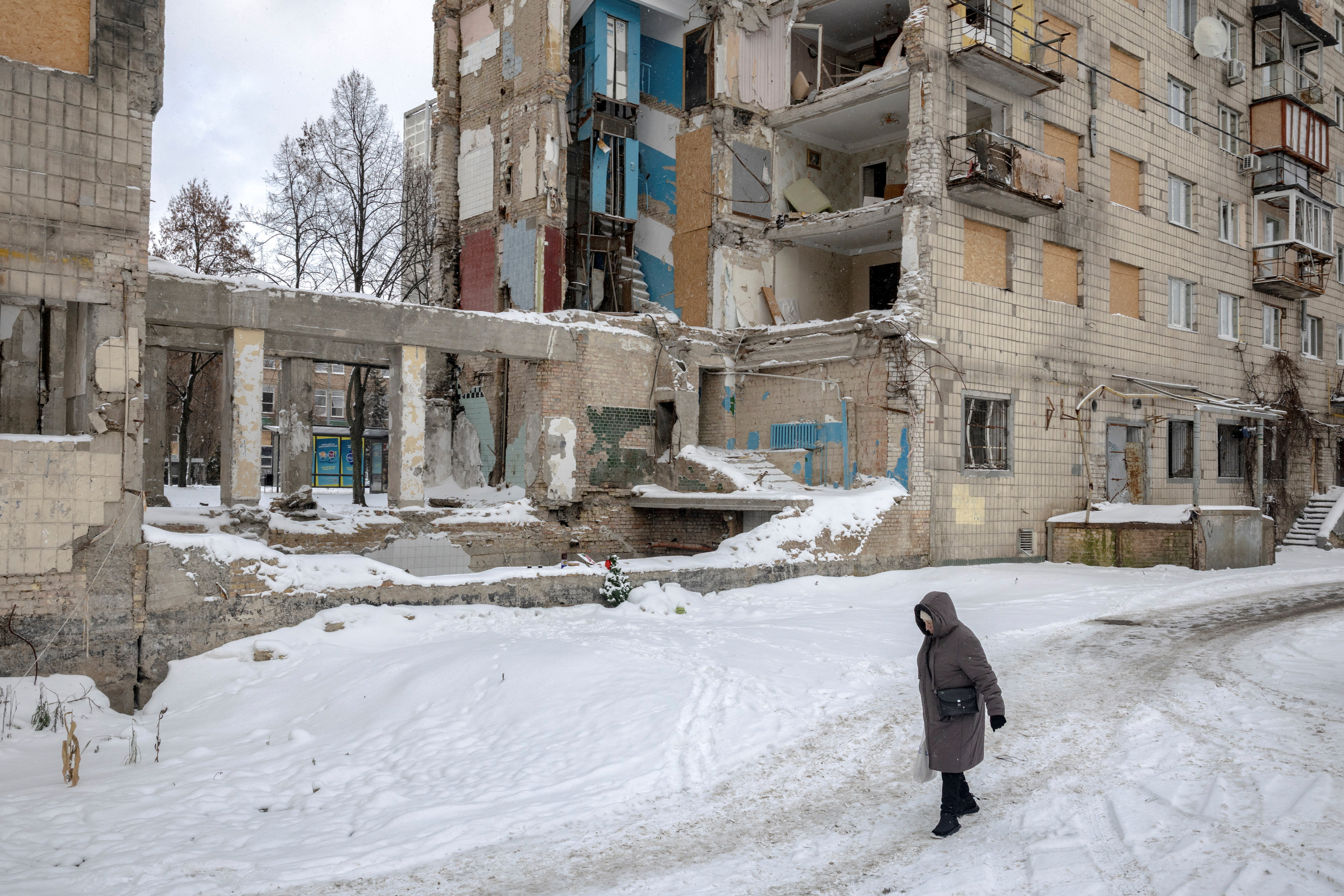 A woman walks on snow, past an apartment building hit by a Russian missile earlier in the year, in Kyiv
