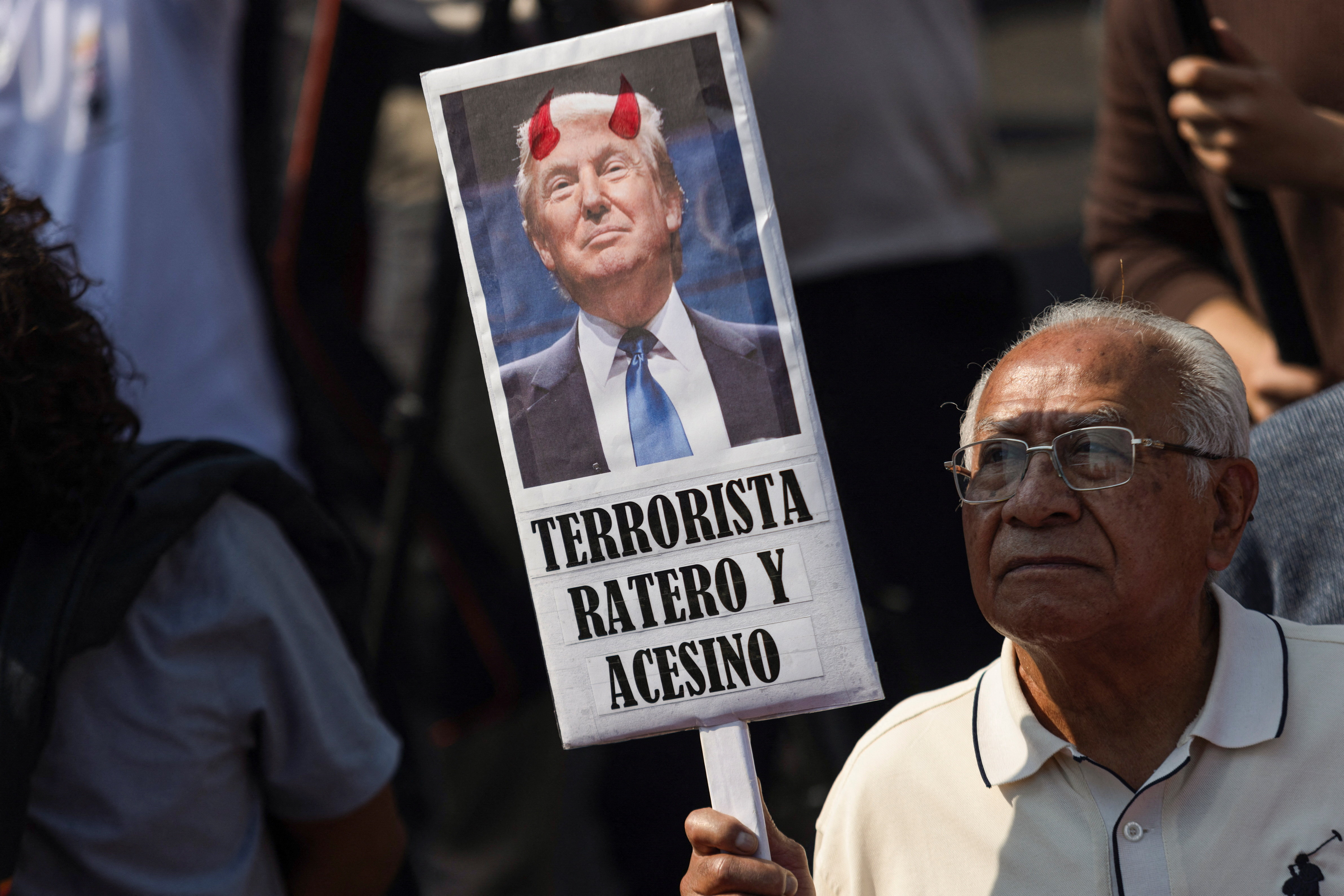 A protester holds a sign with Trump's face that reads, "Terrorista, Ratero Y Acesino"