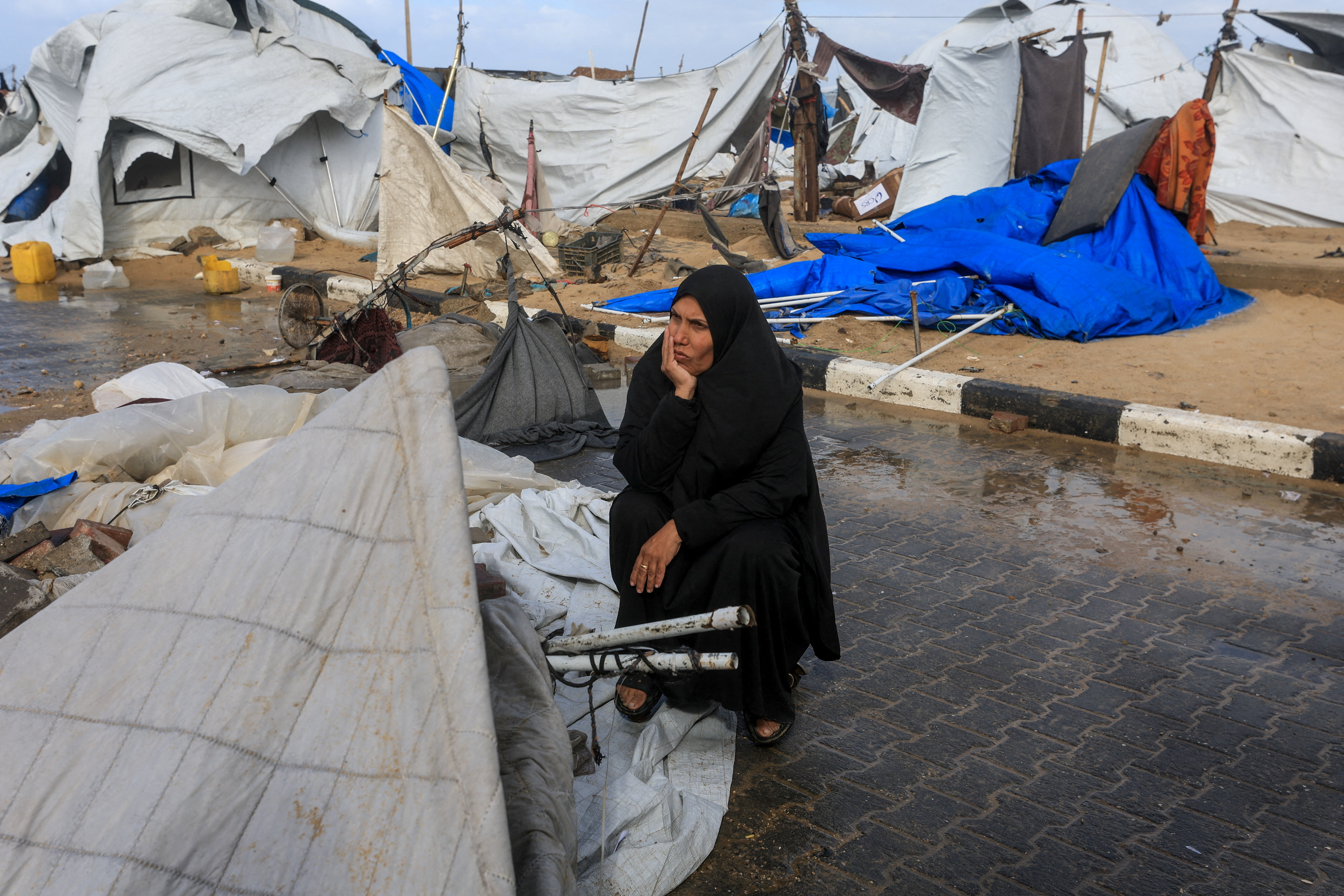 A displaced Palestinian woman sits near damaged tents.