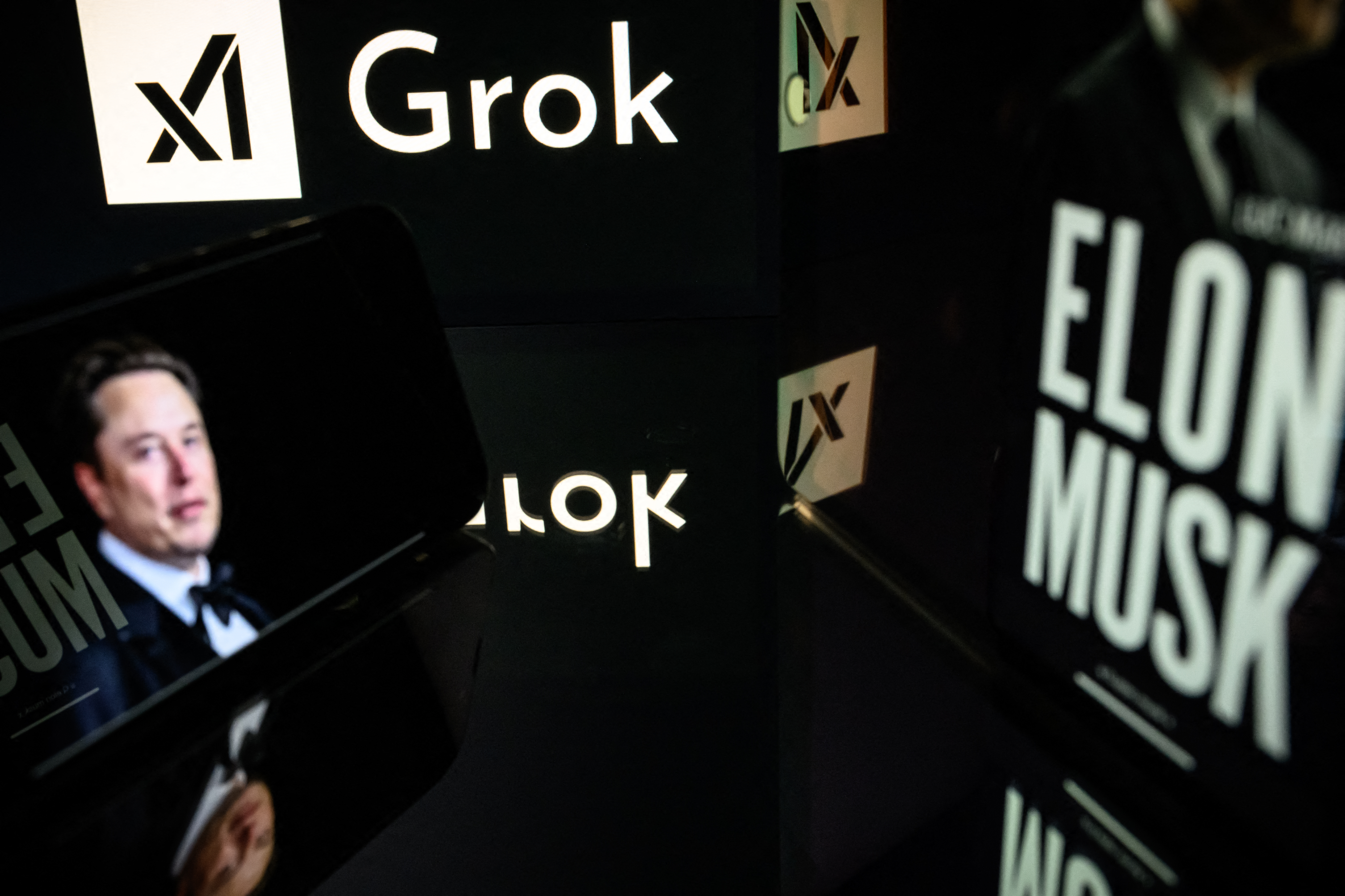 This photograph taken on January 13, 2025 in Toulouse shows screens displaying the logo of Grok, a generative artificial intelligence chatbot developed by xAI, the American company specializing in artificial intelligence and it's founder South African businessman Elon Musk. (Photo by Lionel BONAVENTURE / AFP)