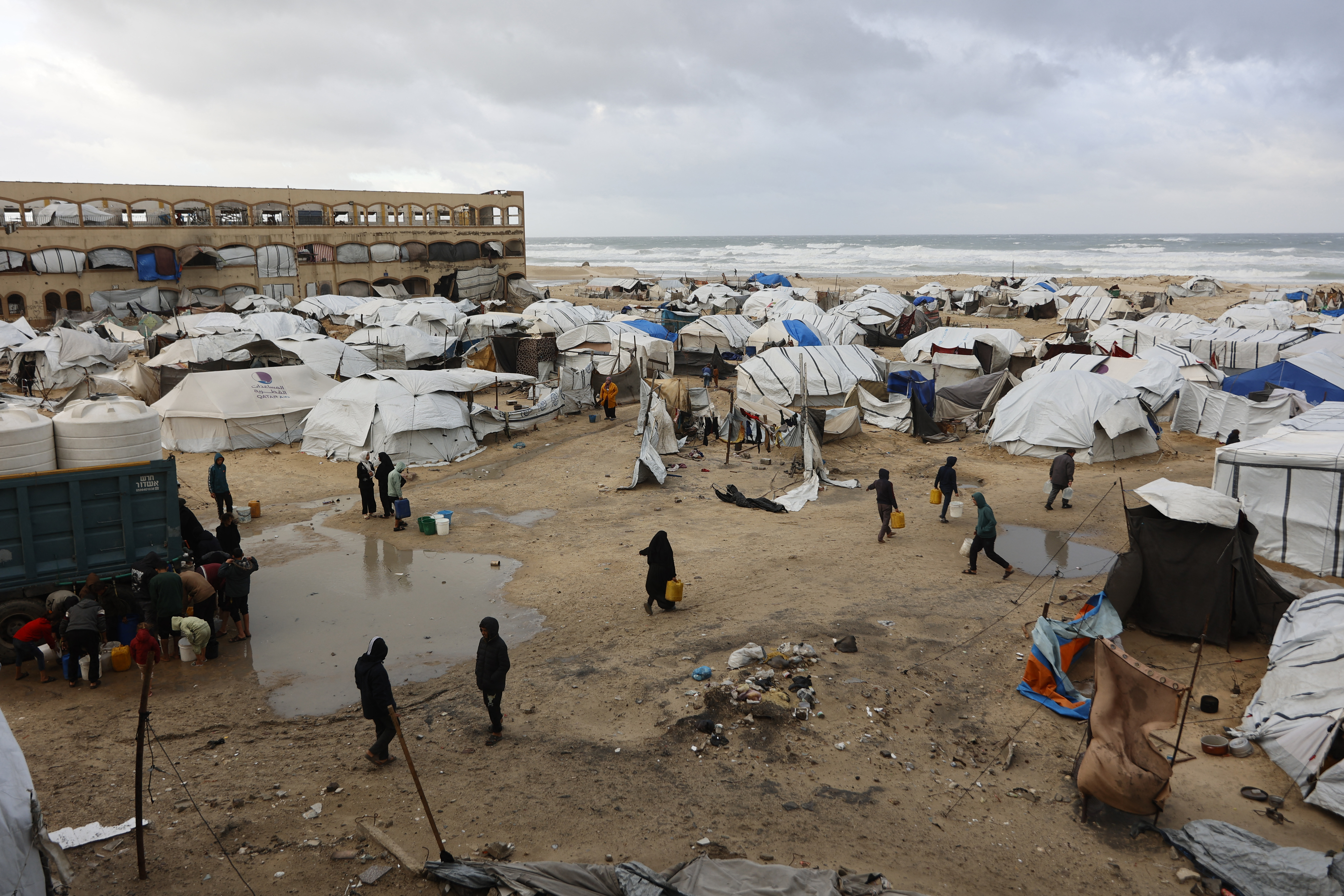 Displaced Palestinians carry jerricans amid tent shelters set up along the shore.