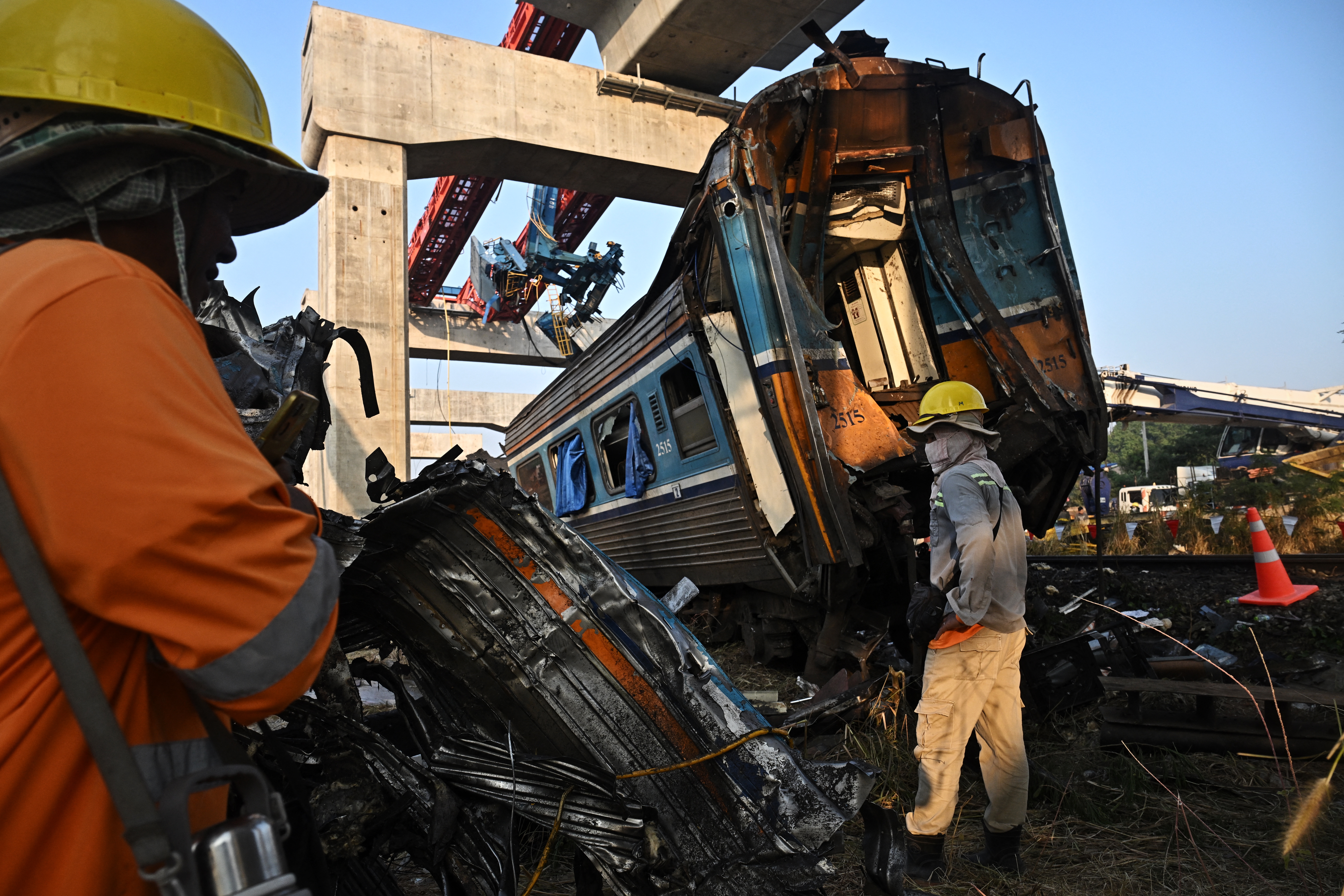 Construction workers look at the wreckage of a train that crashed when a construction crane collapsed the day before, in Thailand's Nakhon Ratchasima province