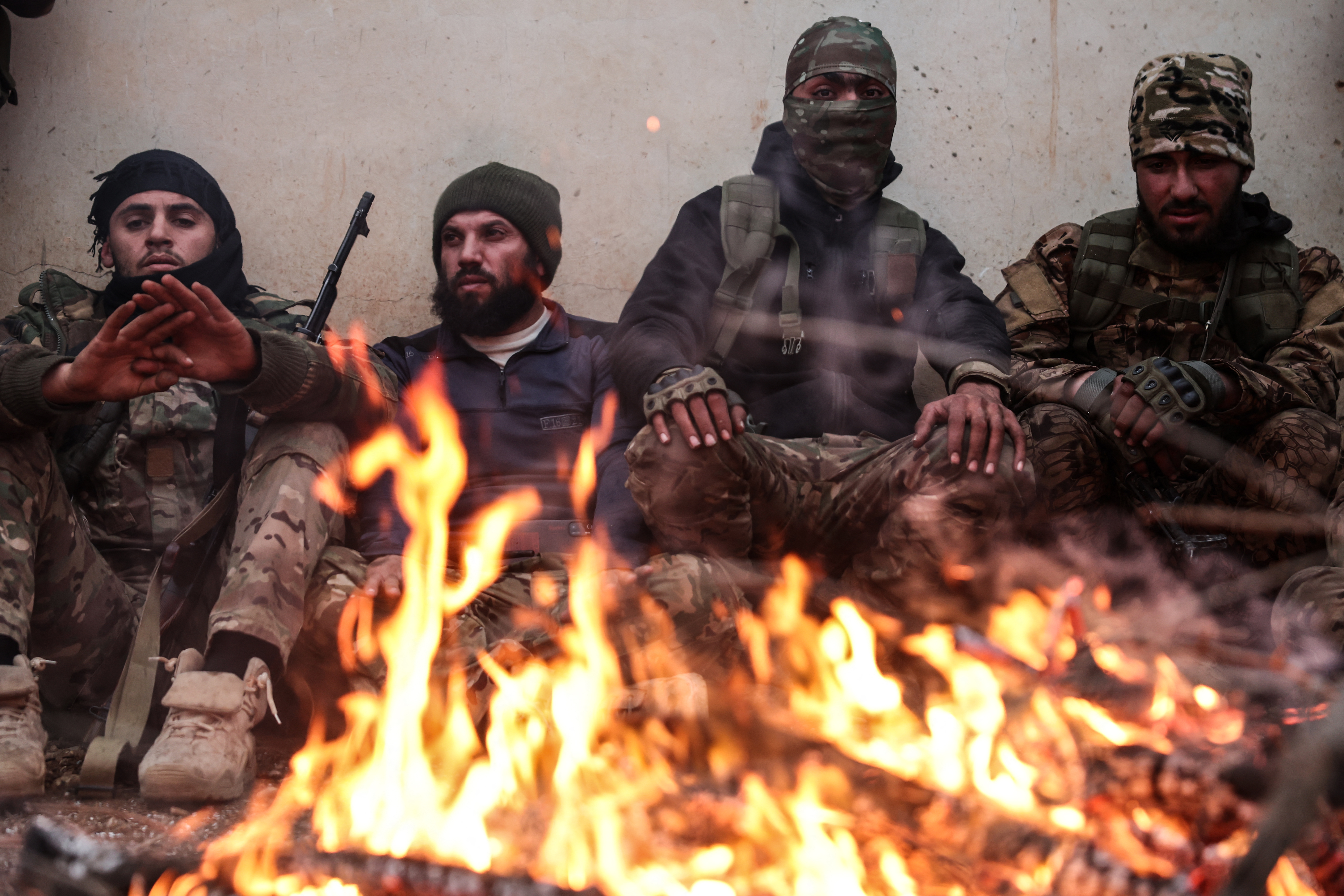 Armed men sit behind a fire.