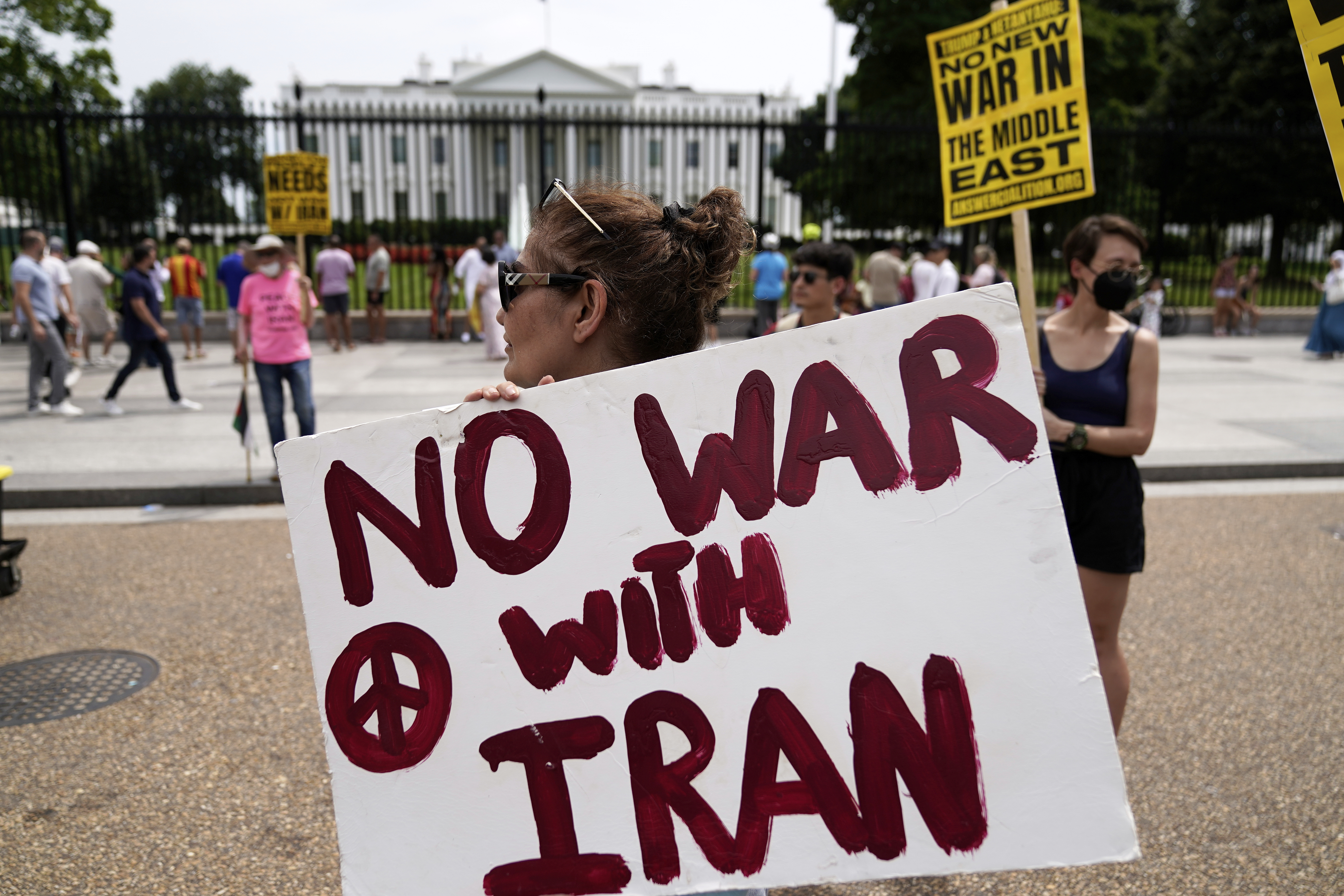 A protester walks by the White House with a sign, "No War With Iran"