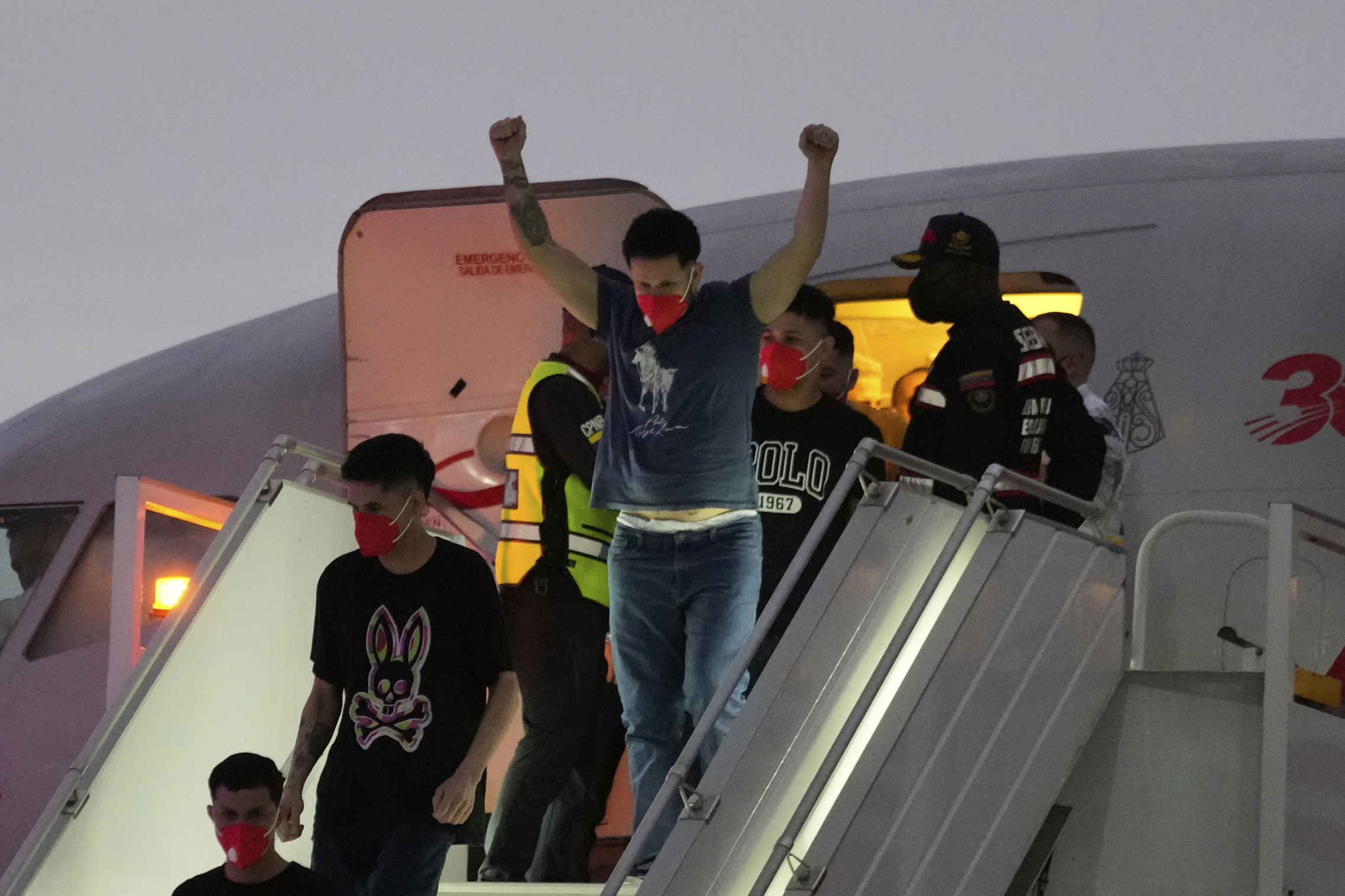 A Venezuelan migrant deported by the US holds up his arms as he descends an airplane in Venezuela