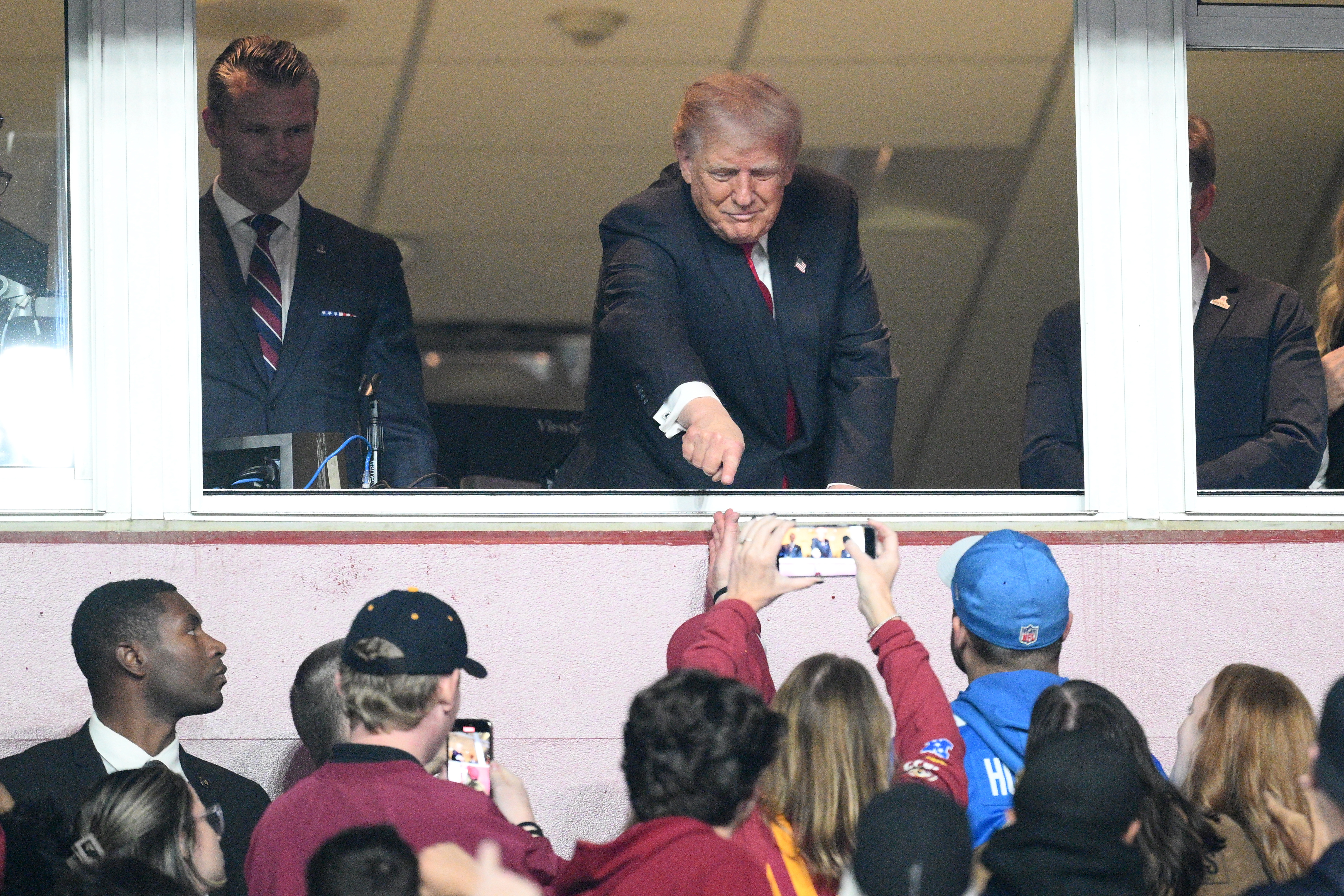 Trump points down to supporters from a box at the Washington Commanders' stadium