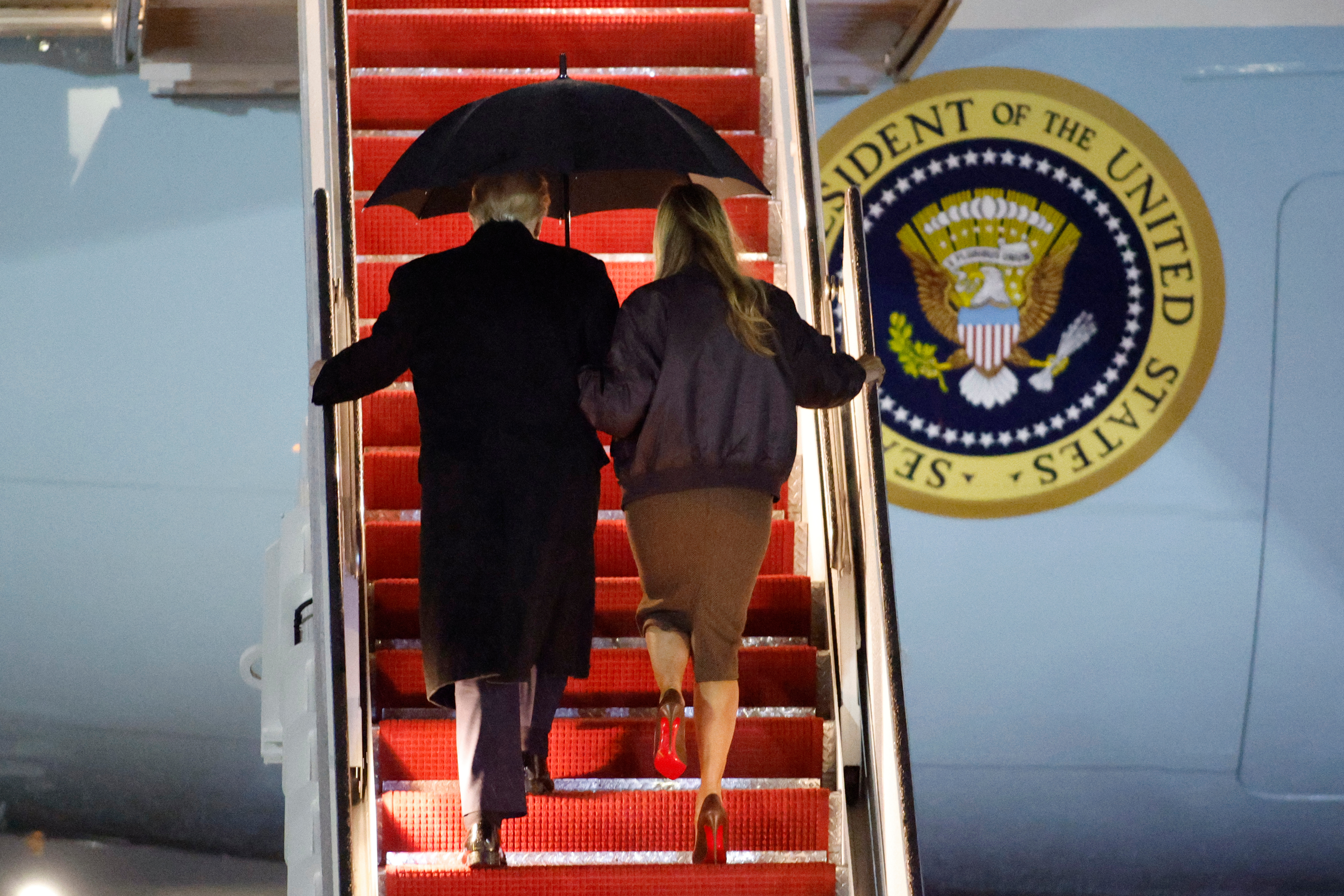 Trump and Melania climb the stairs to Air Force One under a shared umbrella