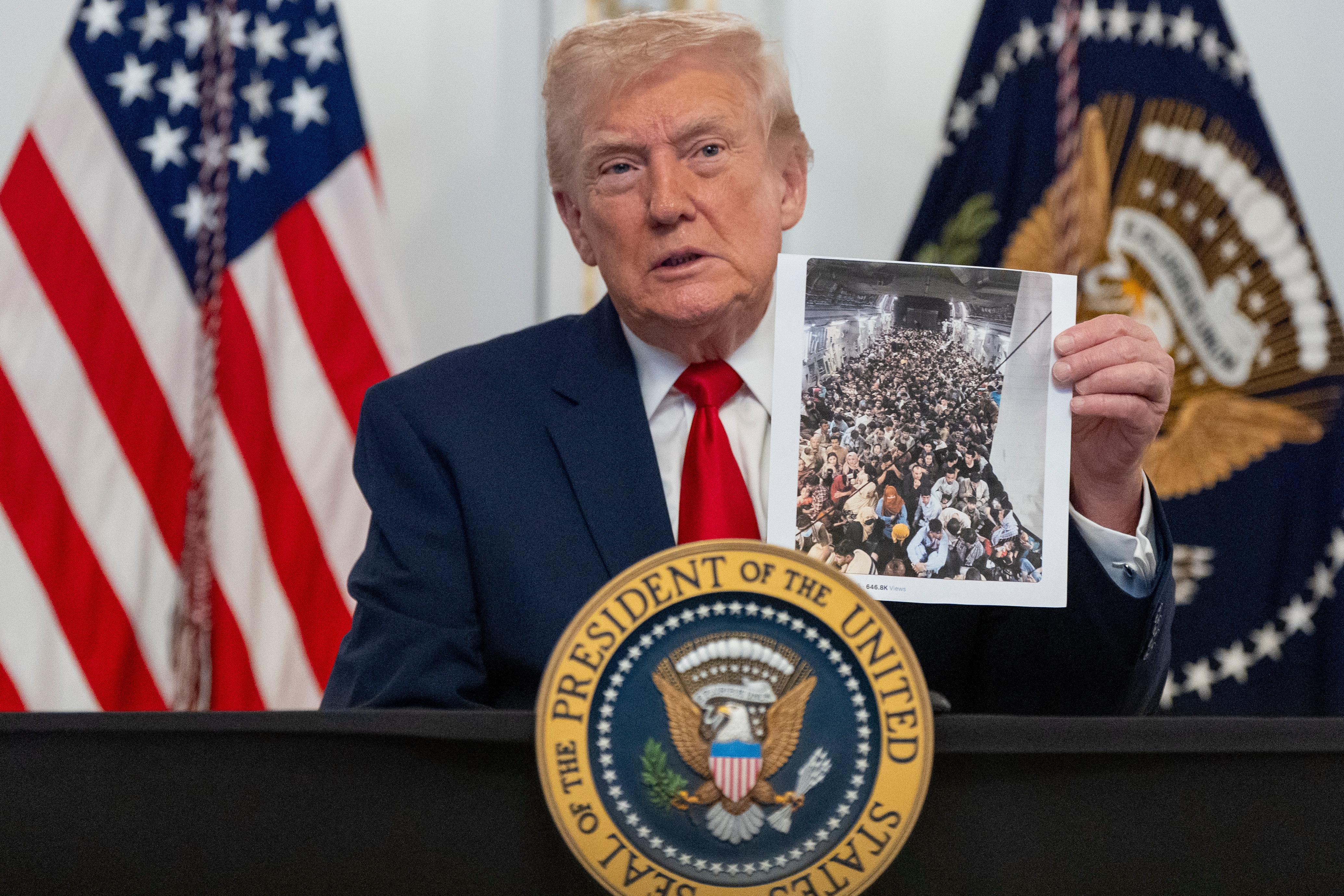 Trump holds up a photo of Afghan refugees from a podium