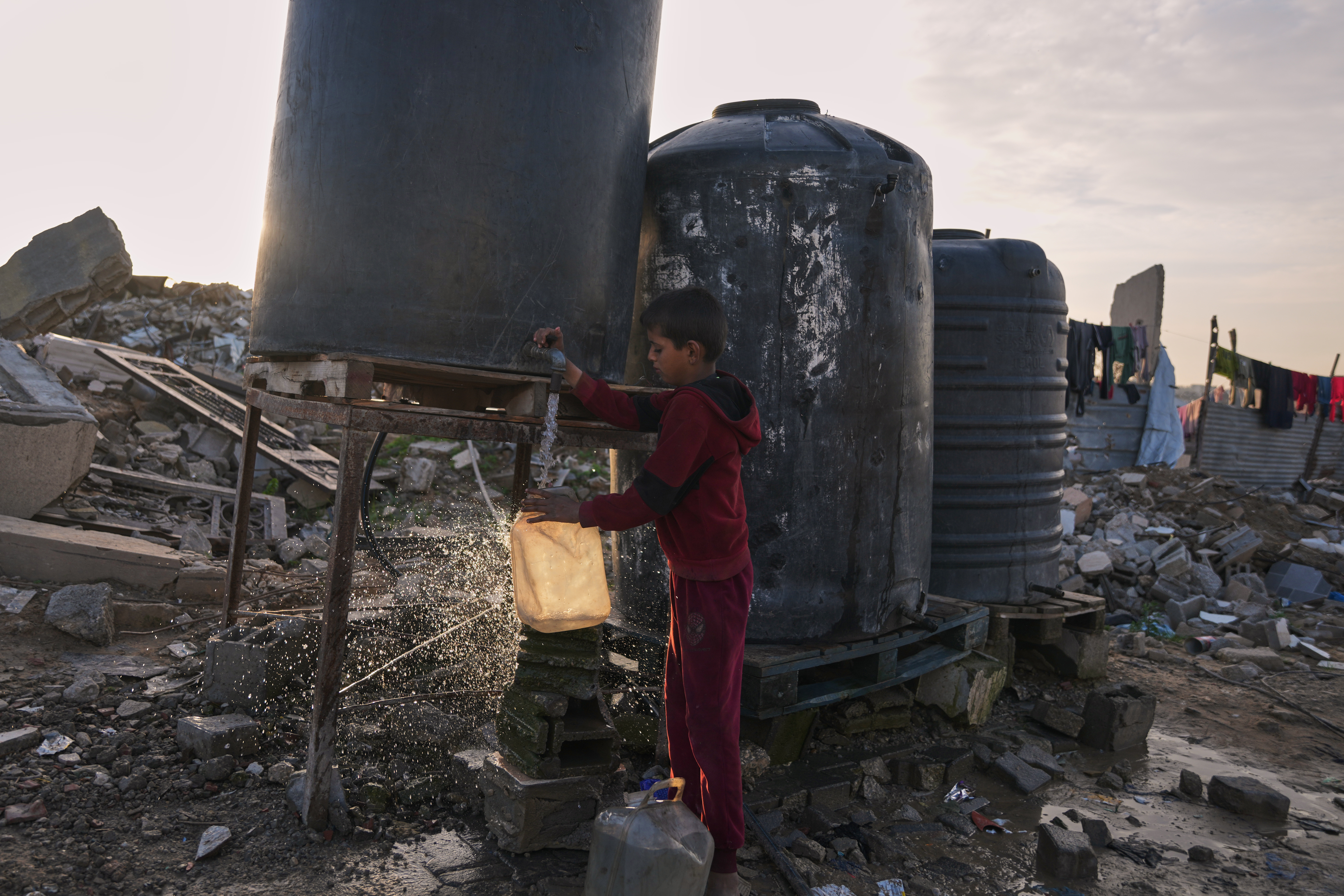 A Palestinian youth collects water from a tank set up in Gaza City, Tuesday, Dec. 30, 2025, amid the rubble of buildings destroyed by Israeli air and ground operations. [File: Jehad Alshrafi/AP]