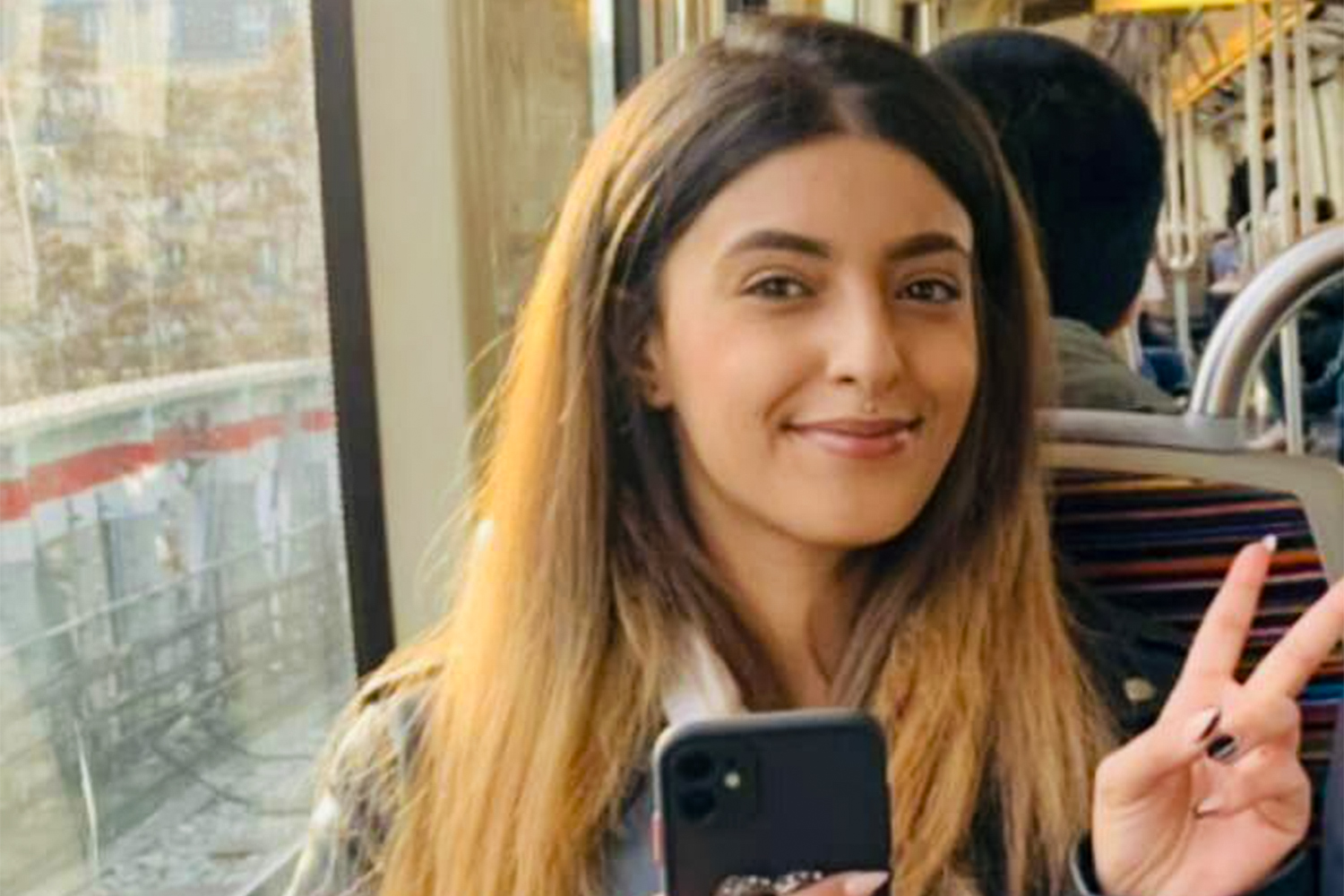 Heba Muraisi smiling, making a victory sign and holding her phone with her other hand.