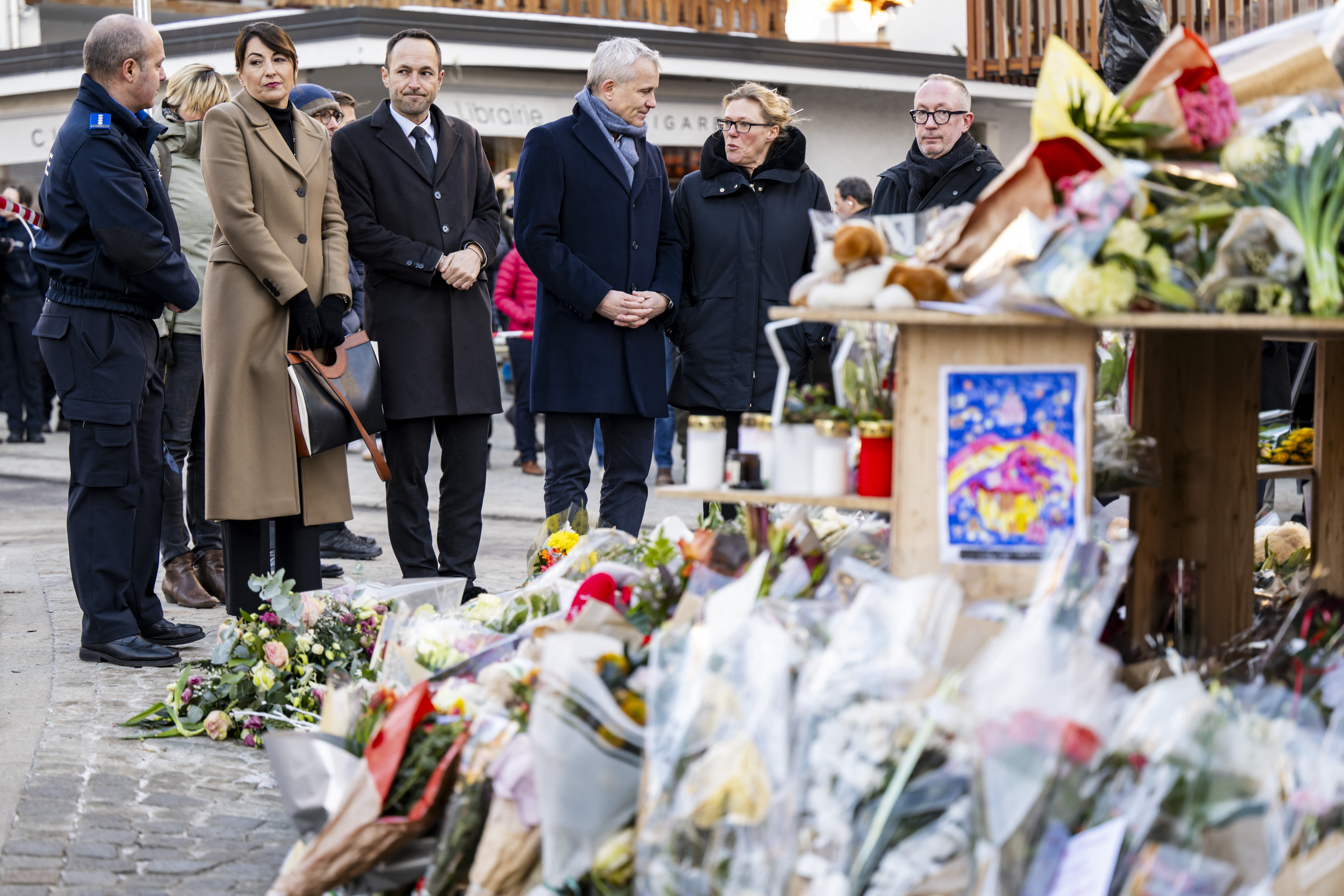 Swiss officials gather at a makeshift memorial in tribute to the victims following a fire at Le Constellation bar during New Year's Eve celebrations in the Alpine ski resort town of Crans-Montana