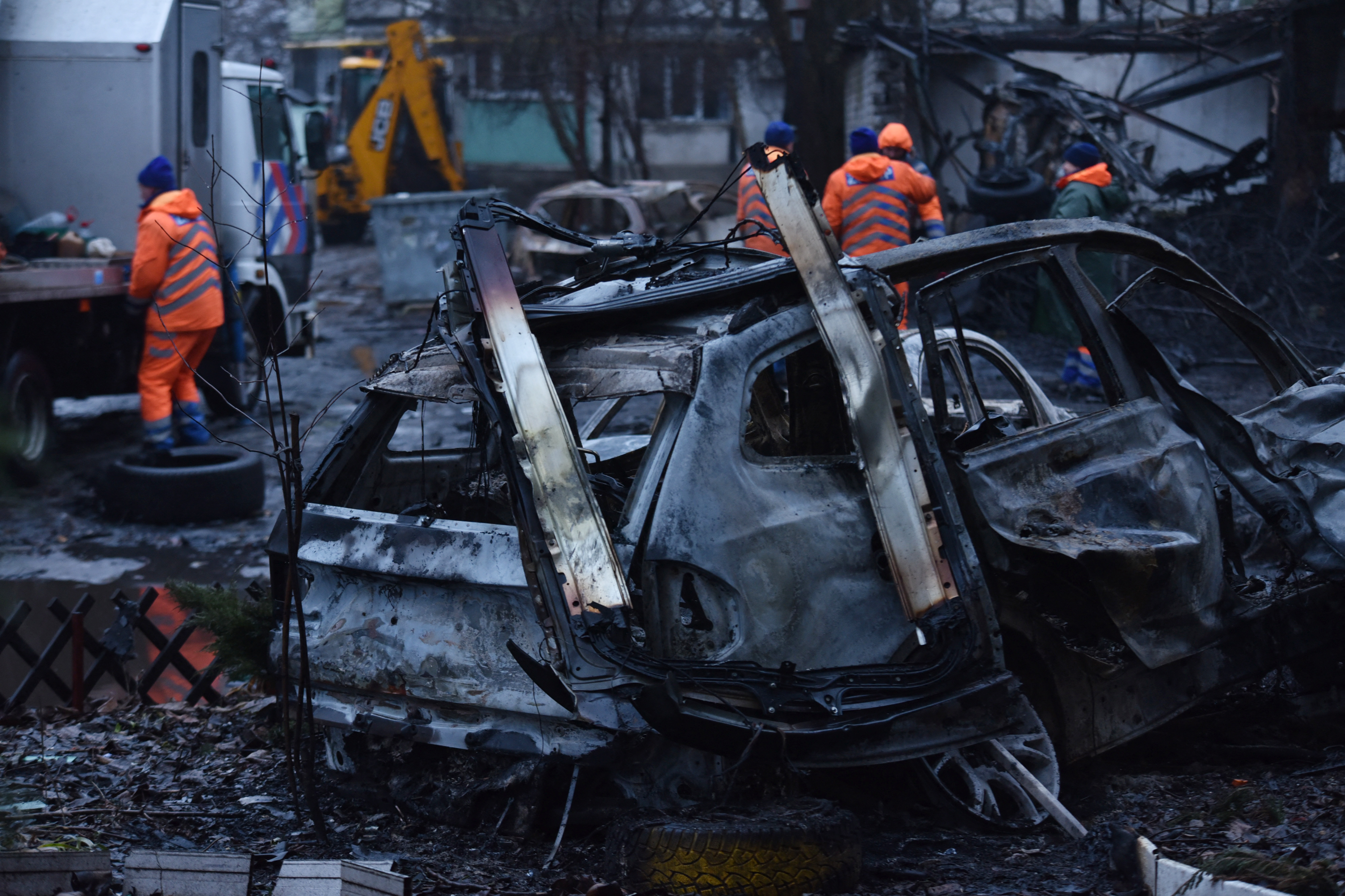 Communal workers clean debris in the courtyard of a damaged residential building next to destroyed cars following a drone attack in Dnipro on January 7, 2026, amid the Russian invasion in Ukraine.