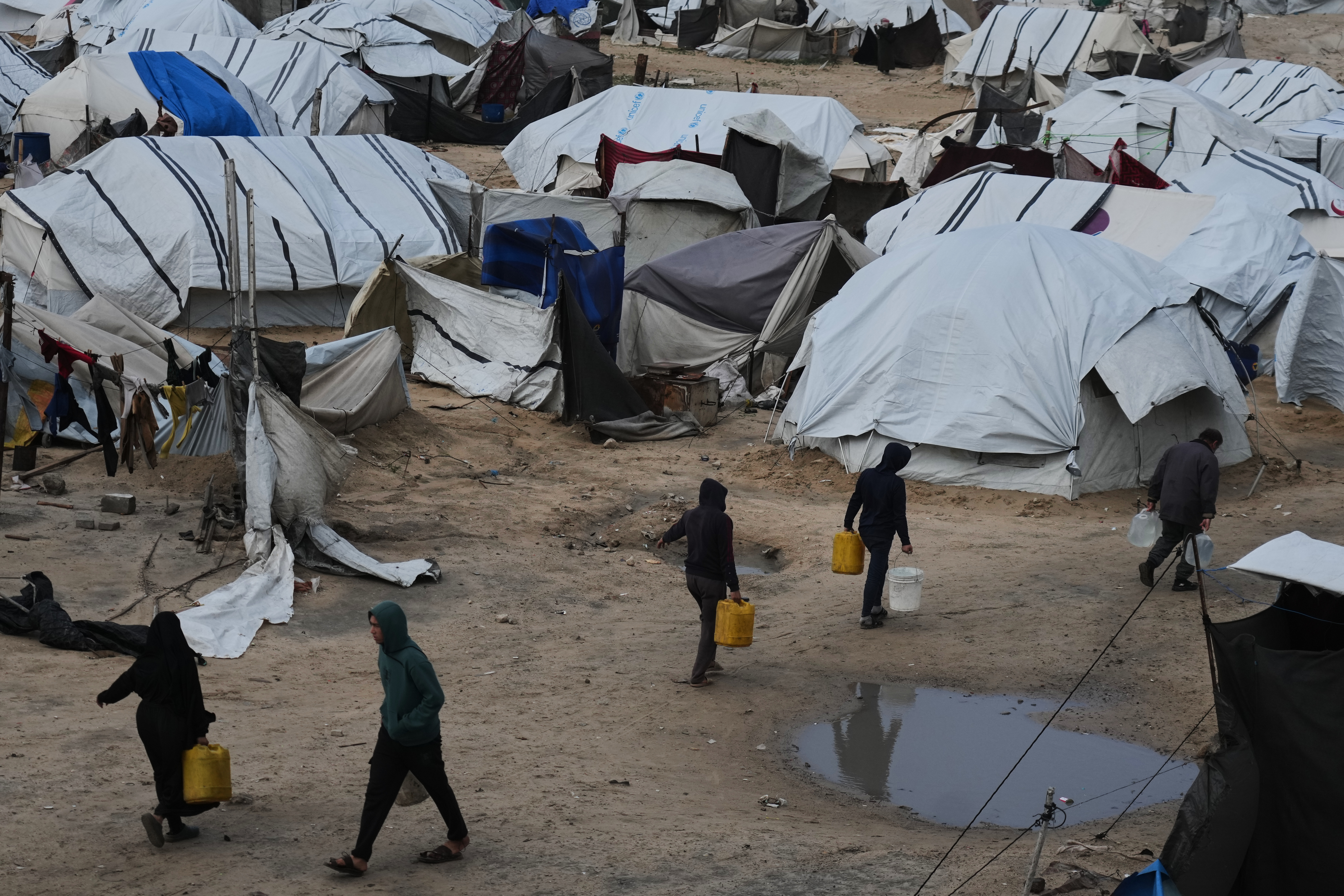 Palestinians carry plastic jerrycans filled with water amid stormy weather at a displacement camp in Gaza City, Tuesday, Jan. 13, 2026. (AP Photo/Jehad Alshrafi)