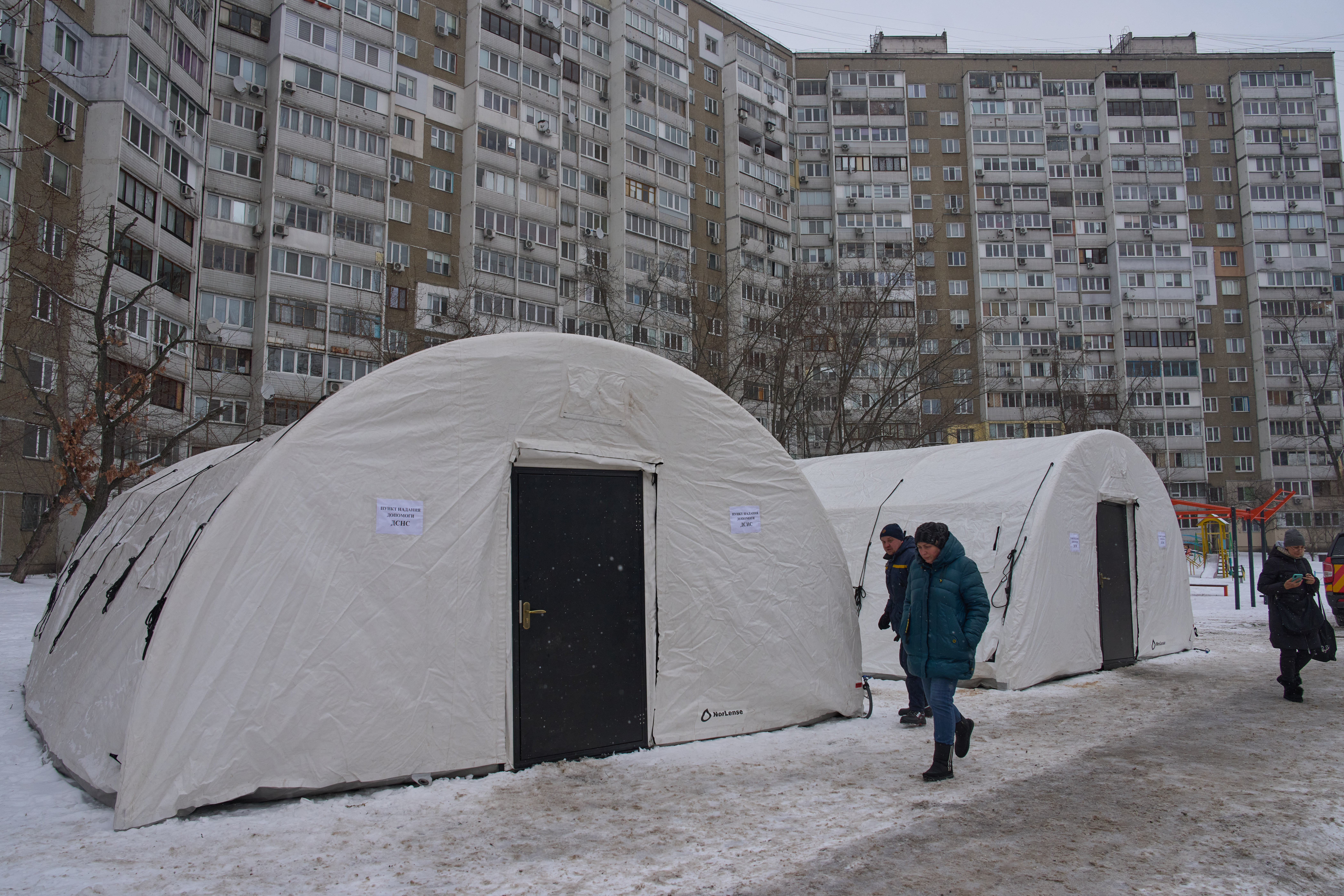 Residents pass by one of emergency tents where people can warm up following Russia's regular air attacks against the country's energy objects, that leave residents without power, water and heating in the dead of winter, in Kyiv, Ukraine, Tuesday, Jan. 13, 2026. (AP Photo/Efrem Lukatsky)