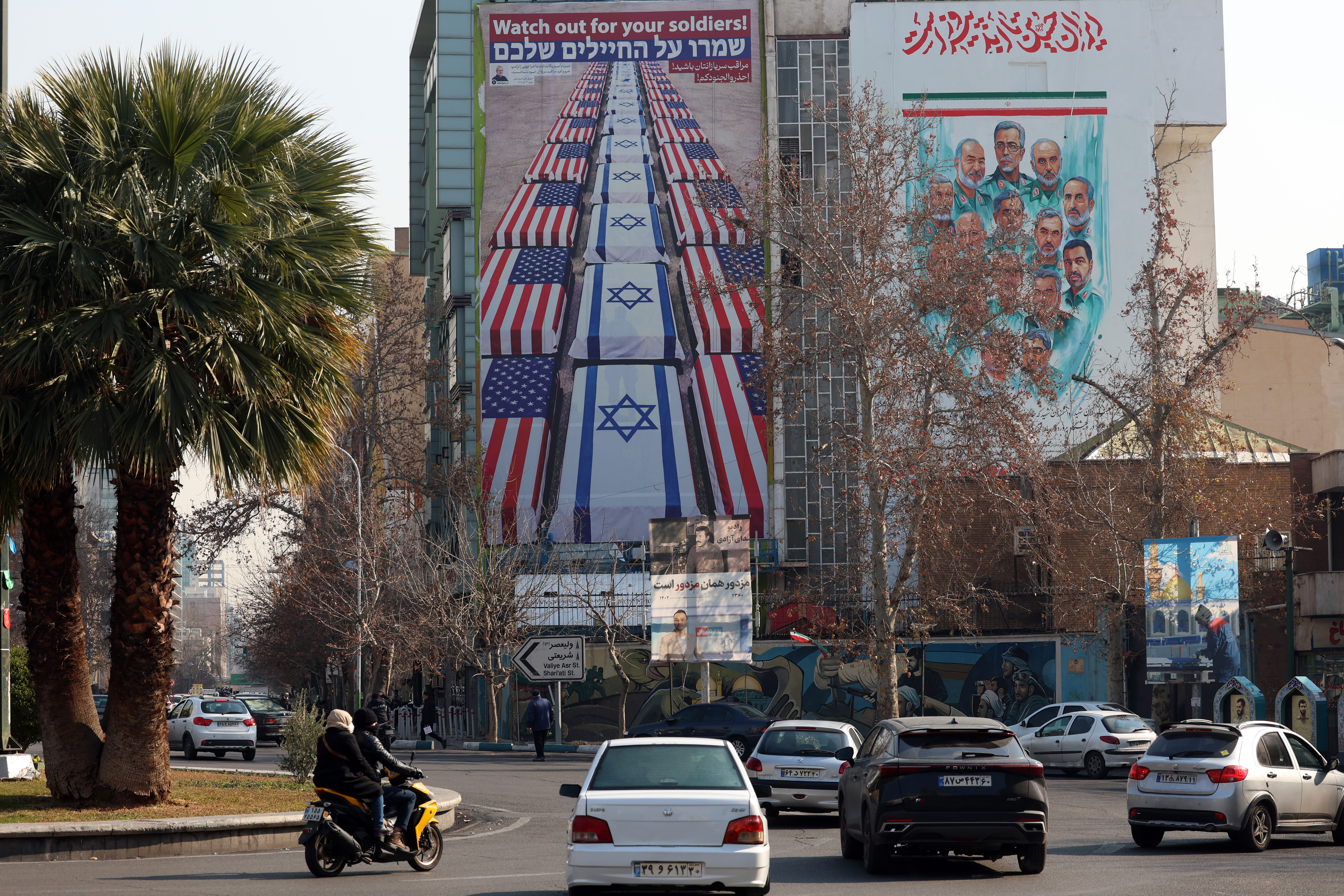 epa12676931 Iranians drive near an anti-US and Israel banner hanging at the Palestine square in Tehran, Iran, 24 January 2026. The US President Donald Trump renewed threats of military action against Iran following anti-government protests. Iran is experiencing a nationwide internet blackout that began on 08 January 2026, amid an intensifying wave of anti-government protests. EPA/ABEDIN TAHERKENAREH