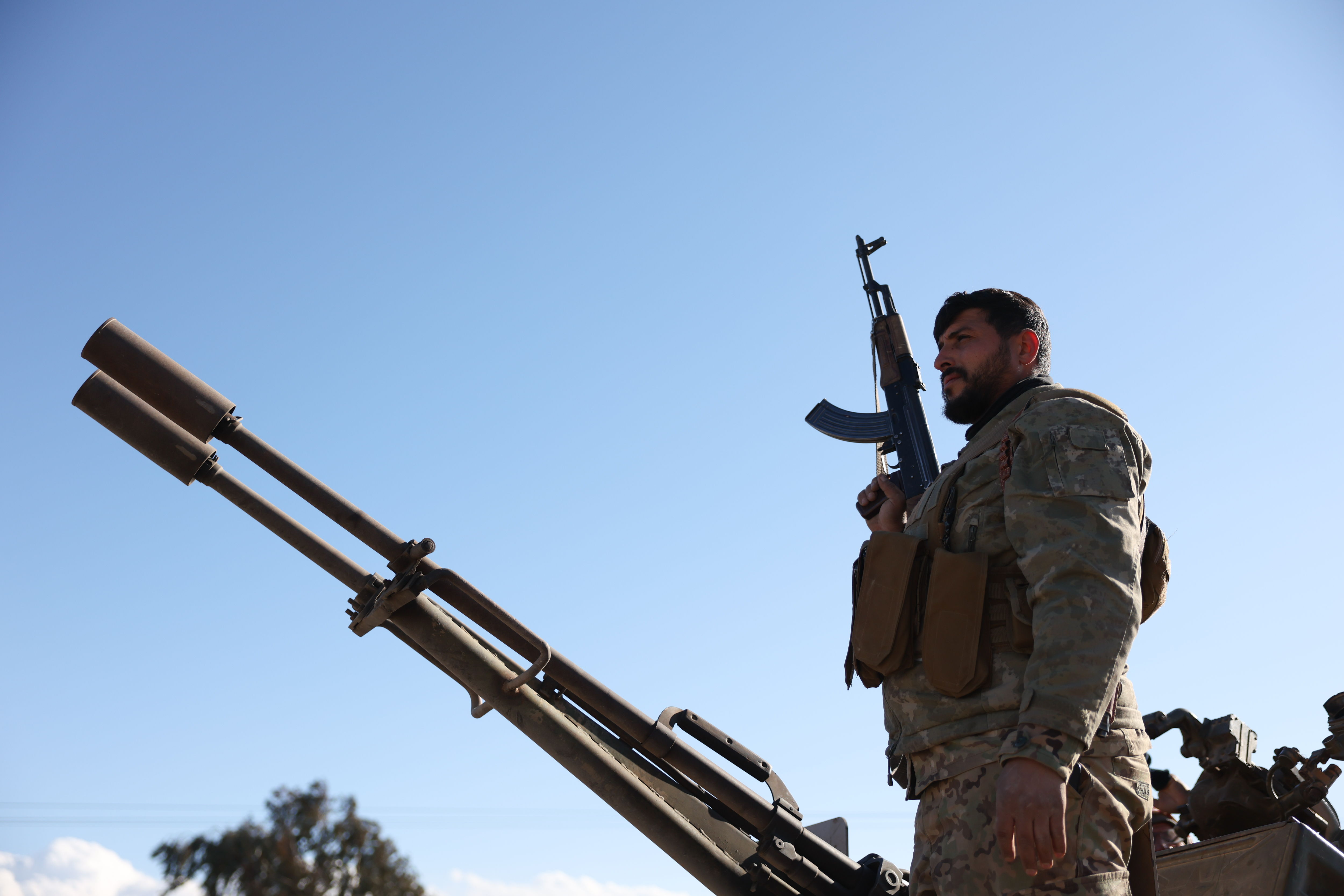 An armed man stands next to a tank.