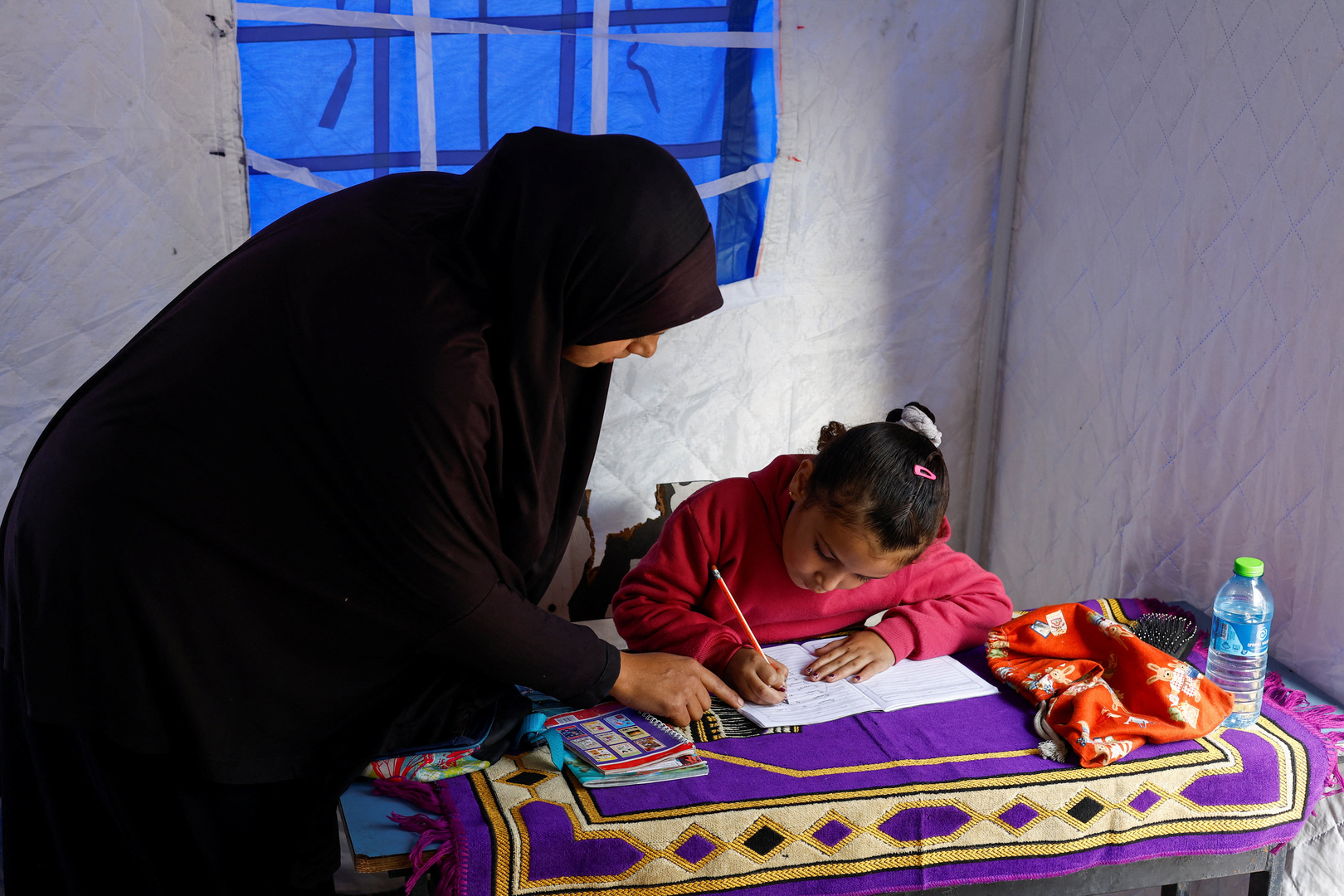 Displaced Palestinian mother, Yasmine Al-Aajouri, helps her seven-year-old daughter Toulin Al-Hindi with her homework inside their tent near the Israeli-designated "yellow line", in Beit Lahiya, northern Gaza Strip on Jan. 6, 2026. [Mahmoud Issa/Reuters]