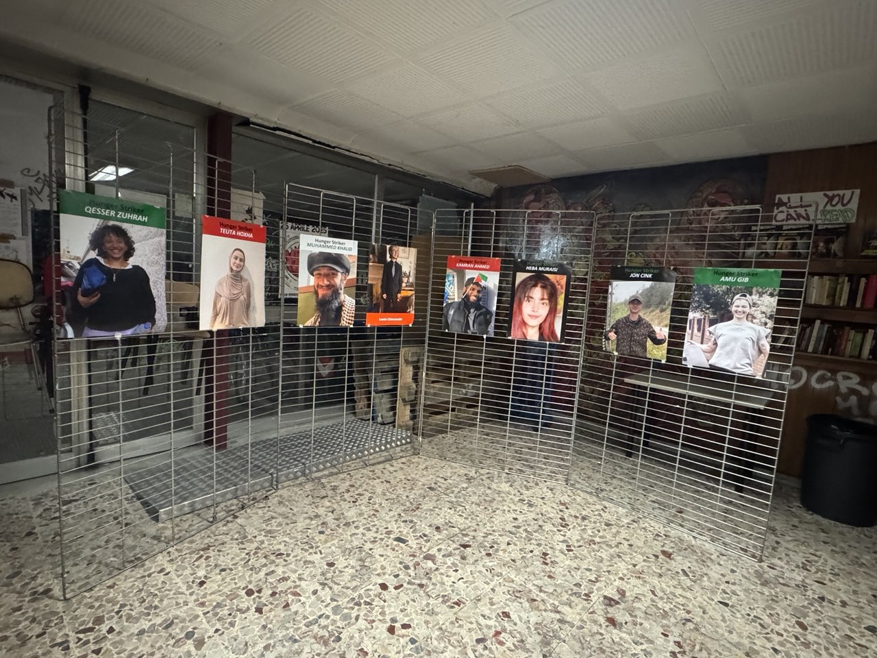 A room with poster with photos of 8 Palestine Action hunger strikers