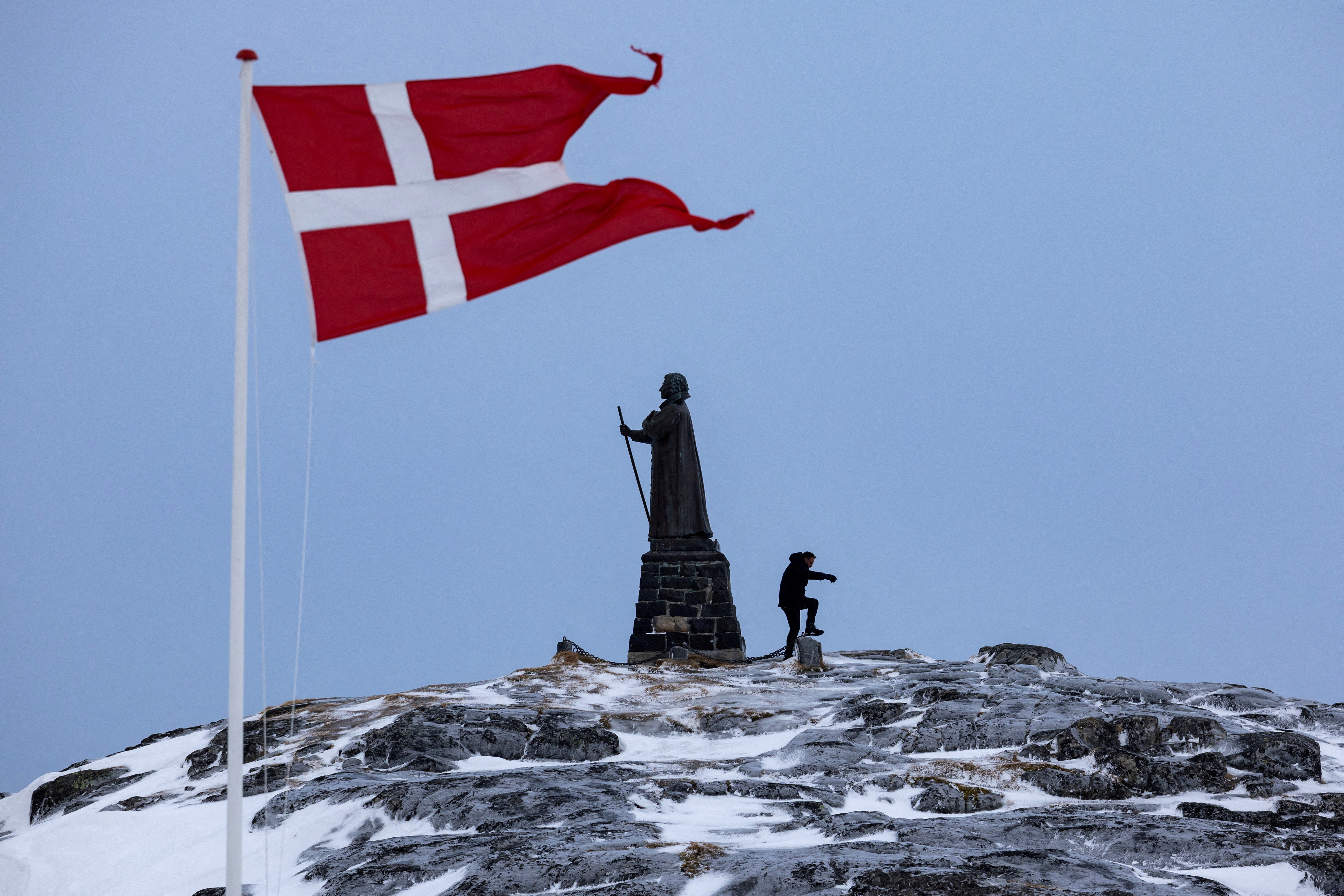 A man walks as Danish flag flutters next to a Hans Egede statue