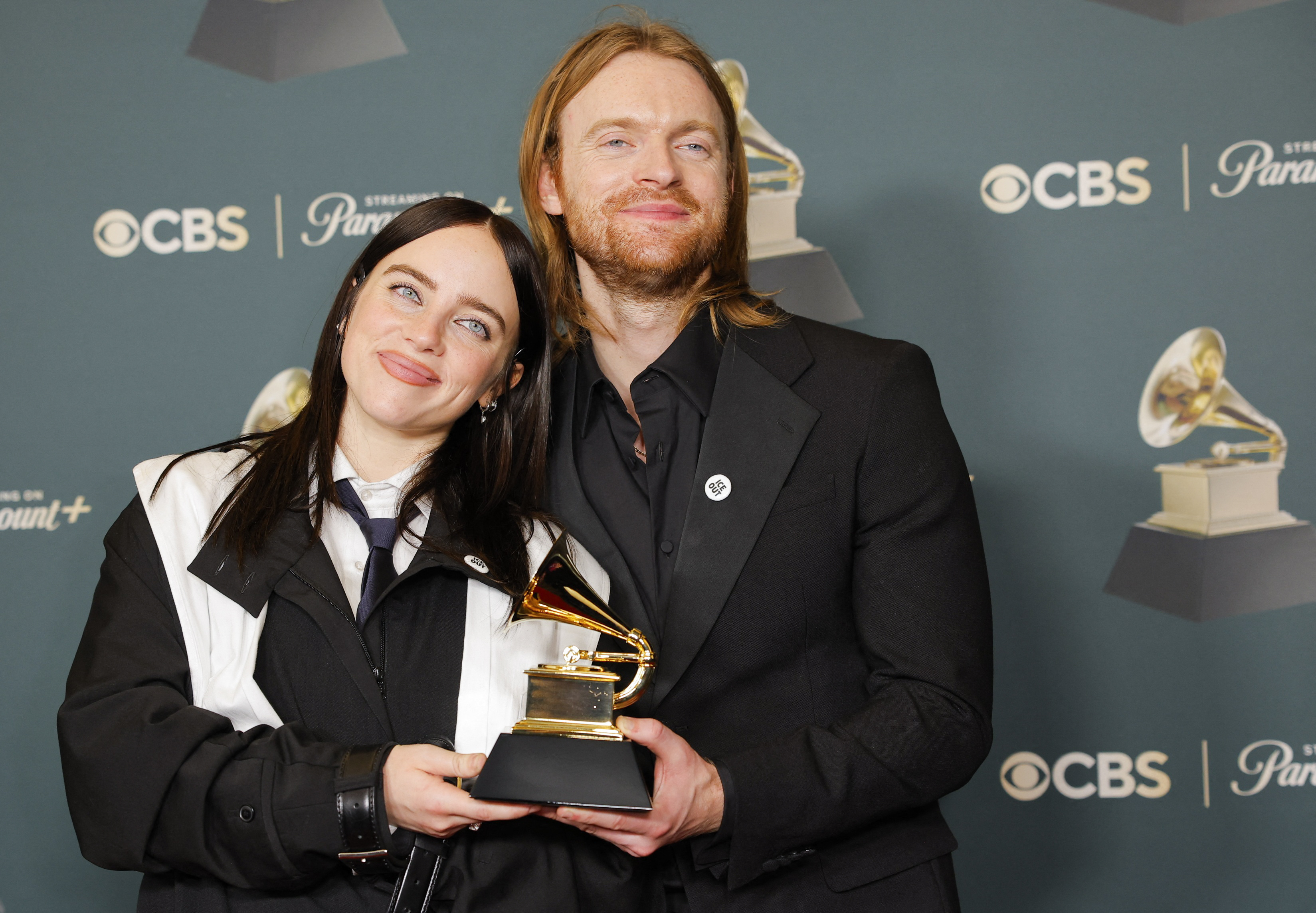 Billie Eilish and Finneas wearing ICE Out pins pose with the award for Song of the Year for "WILDFLOWER"