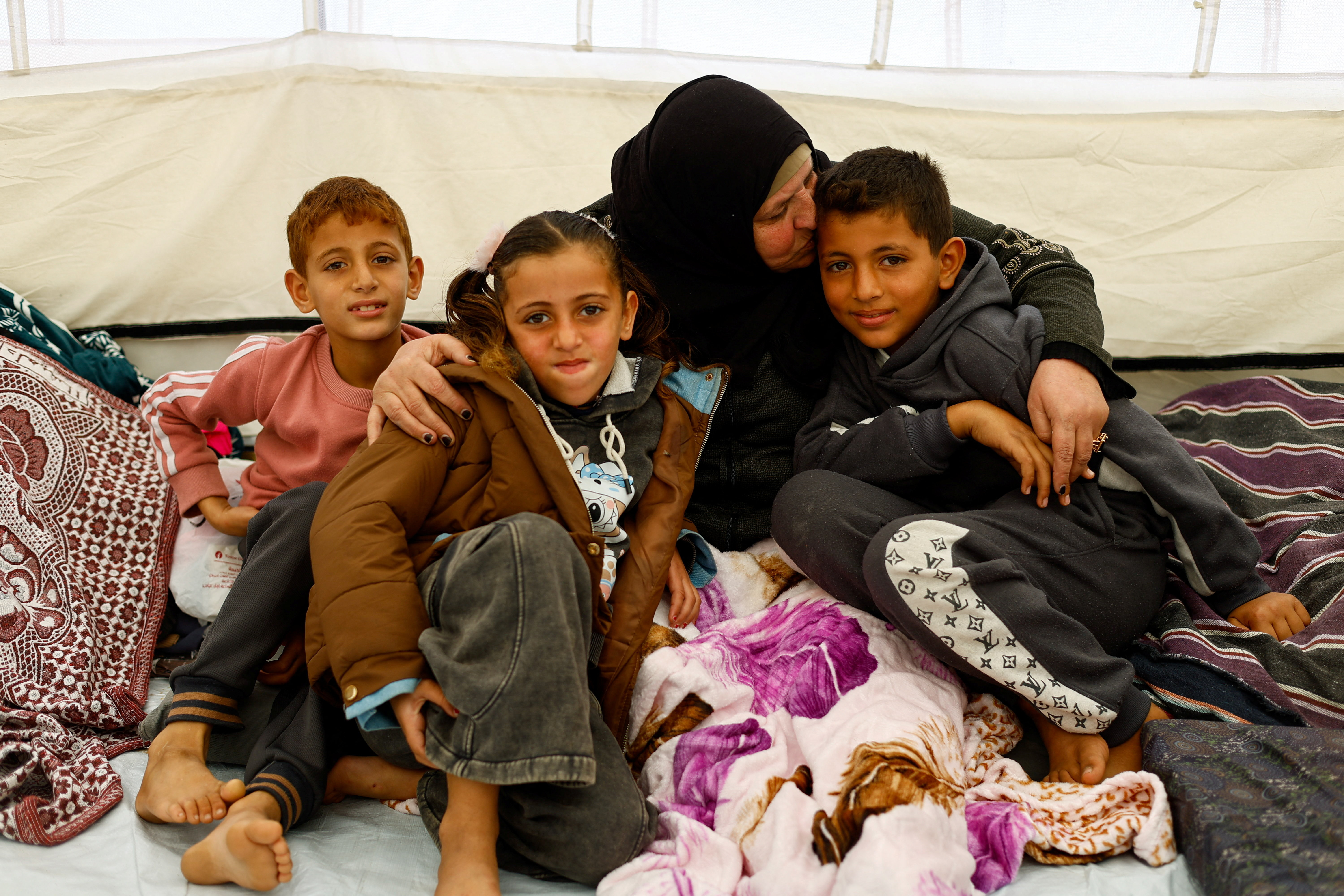Huda Abu Abed, 56, hugs her grandchildren at a tent shelter after returning to Gaza through the Rafah crossing, in Khan Younis in the southern Gaza Strip, February 3, 2026. REUTERS/Mahmoud Issa